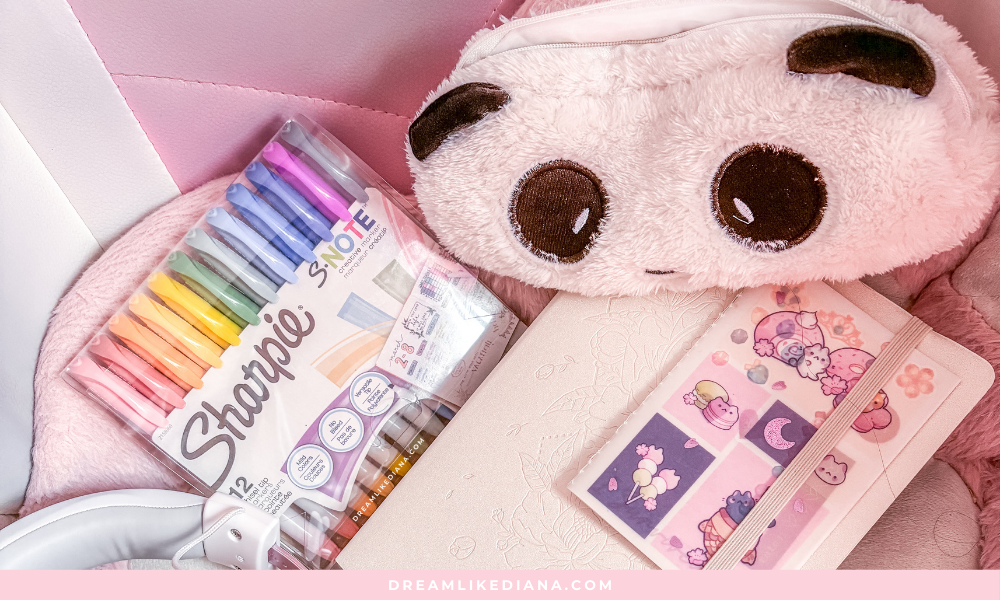 A cozy creative setup showing pastel Sharpie markers, a fluffy panda pencil case, a beige notebook, and a pink notebook with cute stickers.