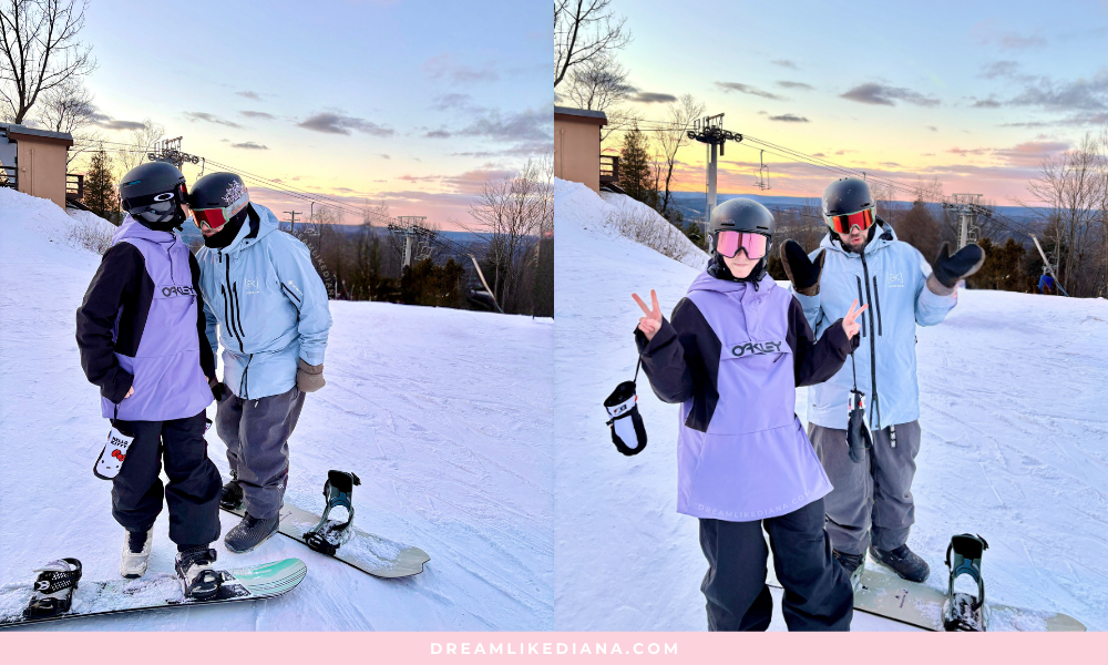 Two snowboarders in helmets and goggles pose playfully on a snowy slope at sunset. A picturesque view and ski lift are visible in the background.