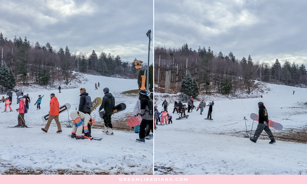 A snowy hillside with people carrying snowboards and skis. The scene is lively, with children and adults preparing to enjoy winter sports under a cloudy sky.