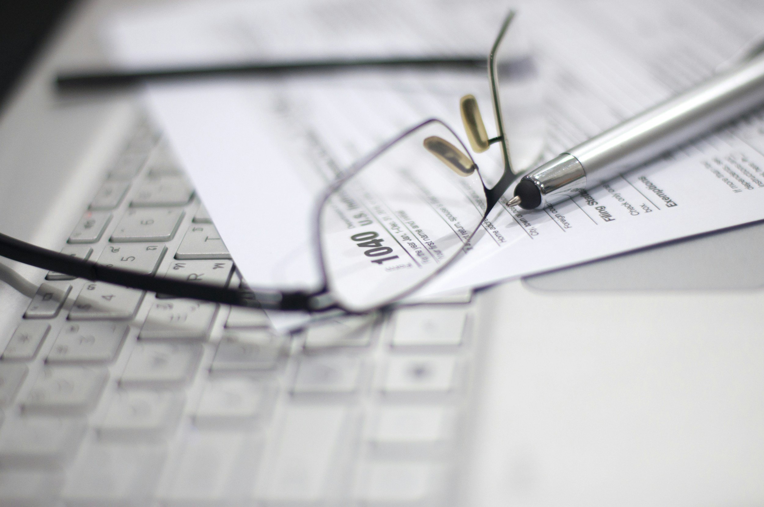 Close-up of eyeglasses, a pen, and printed receipts on a white keyboard and desk.