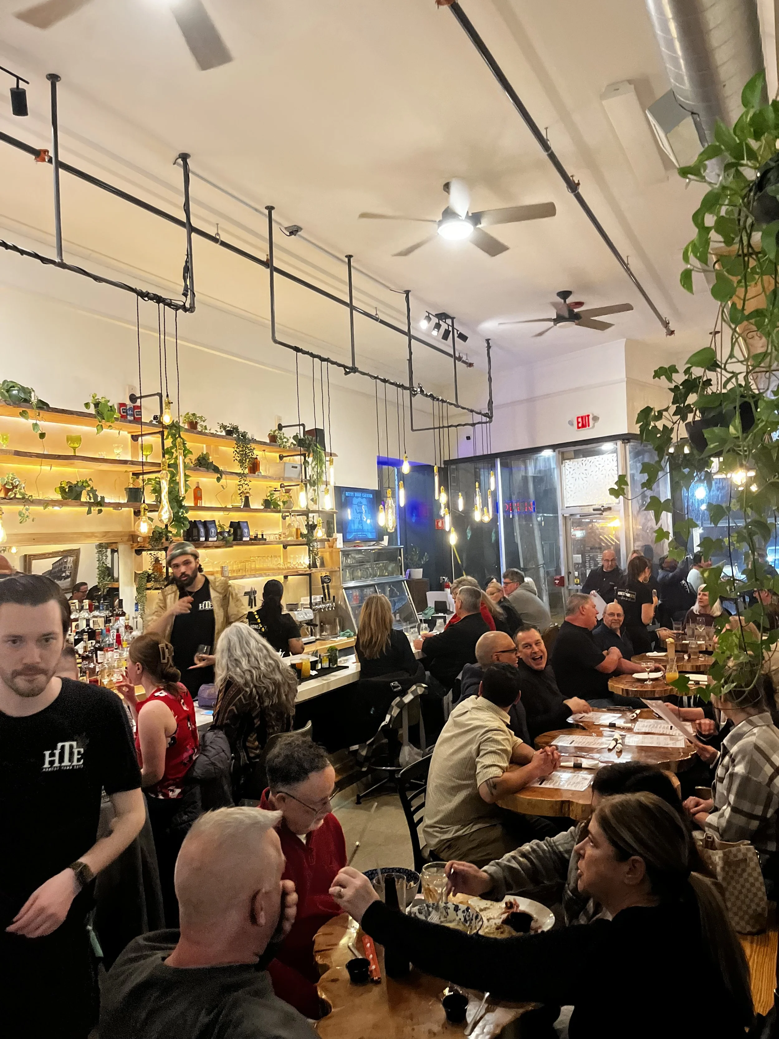 Honest Town Eats, a busy restaurant interior with patrons seated at tables and a bar area, with hanging lights and a decorated wall.