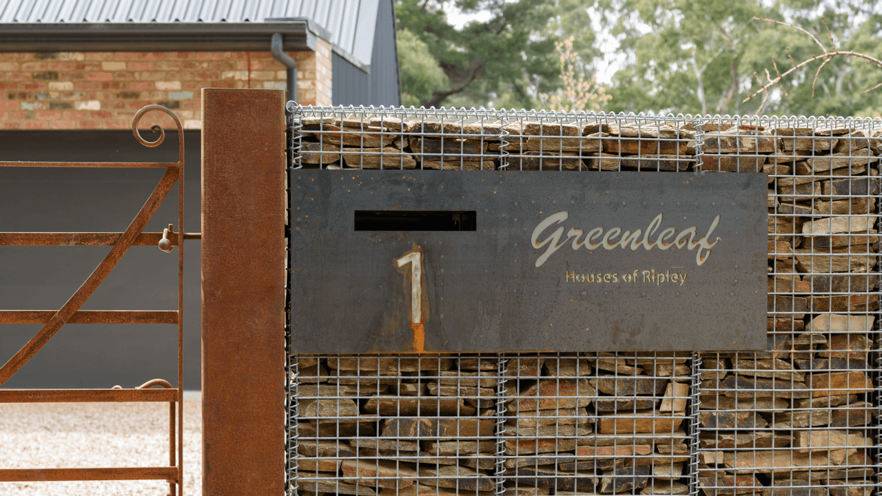Rusty metal gate and fence with a sign reading 'Greenleaf Houses of Ripley' and the number 1, with a brick building and trees in the background.