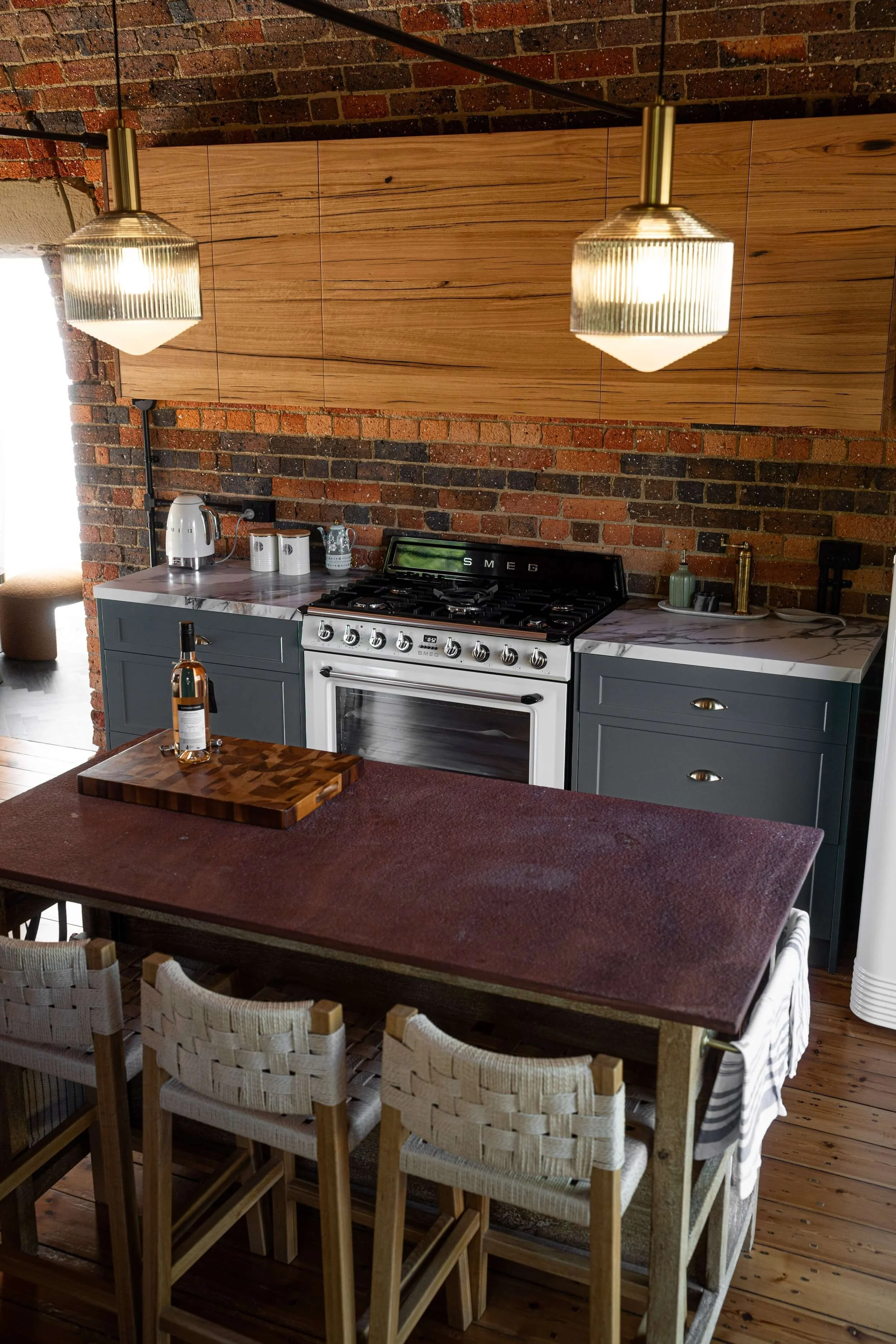 A kitchen with brick walls, a marble-topped counter, a white stove, and a wooden dining table with woven chairs.