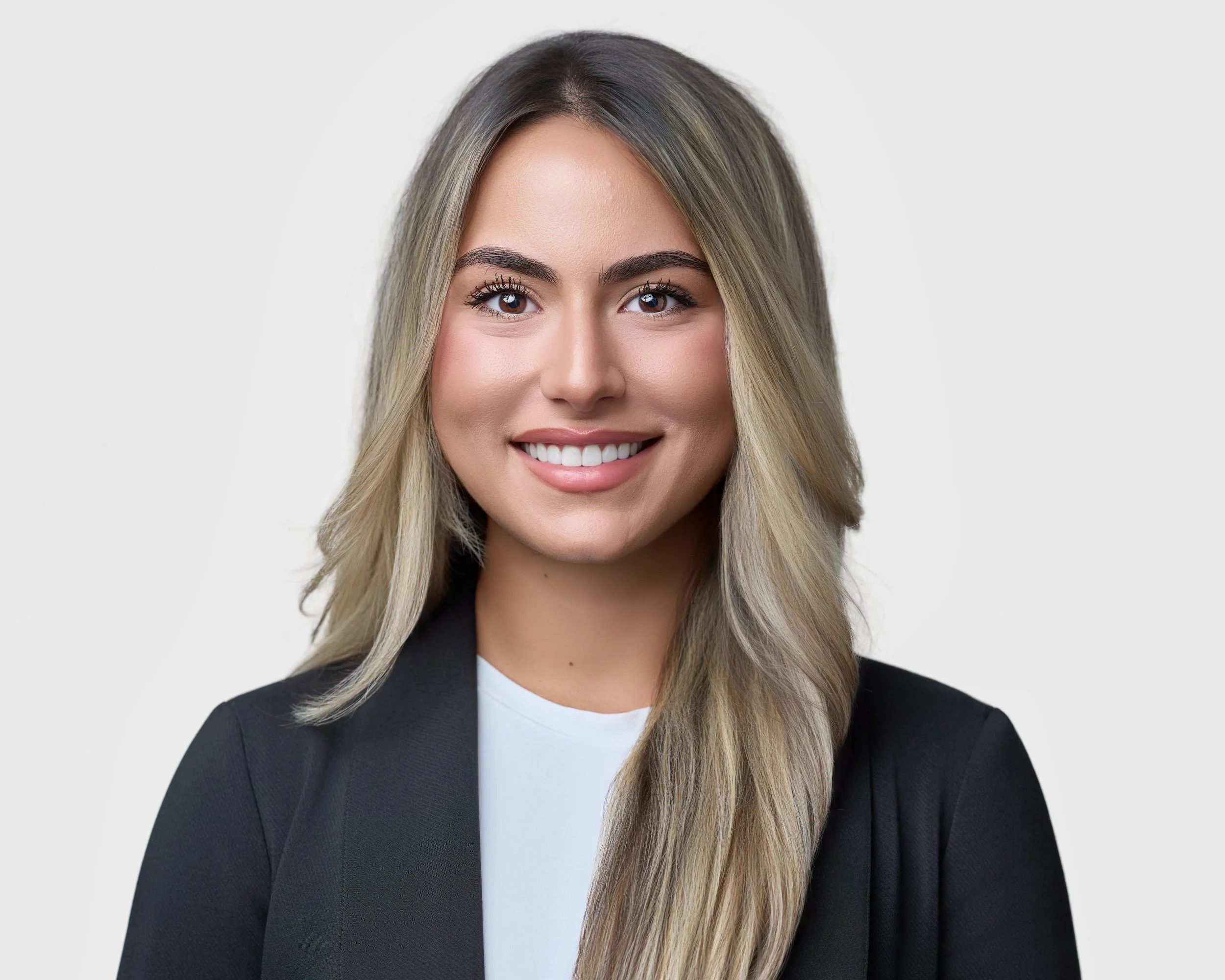 A smiling woman with long blonde hair, wearing a black blazer and white top, against a plain light background.
