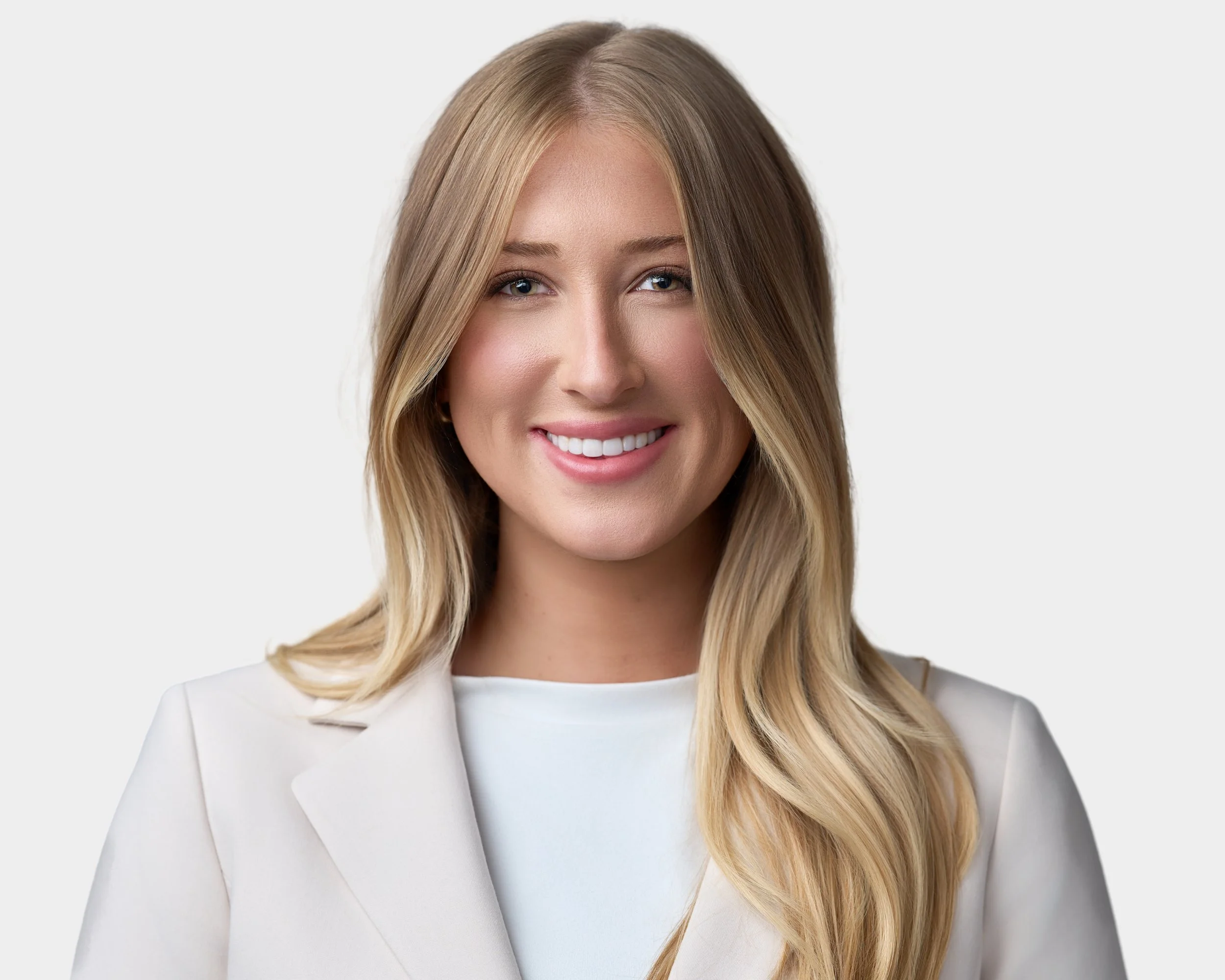 Headshot of a smiling woman with long blonde hair wearing a white blazer and white top against a plain light background.