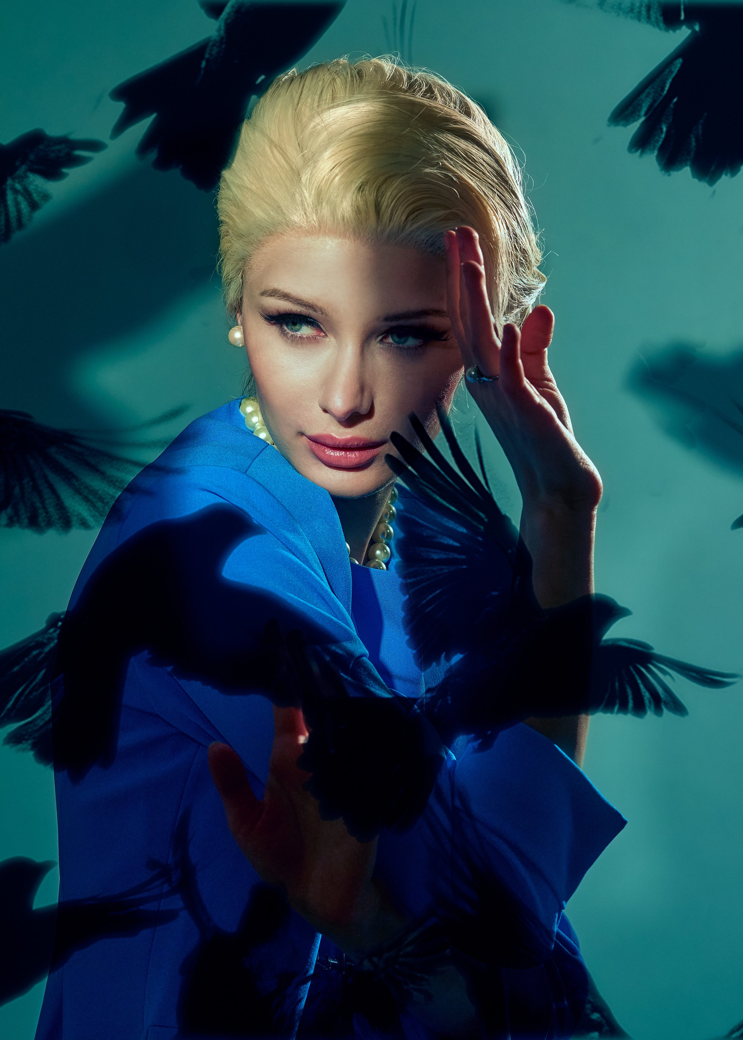 A woman with blonde hair wearing a blue outfit, pearl earrings, and a pearl necklace surrounded by black birds in flight.