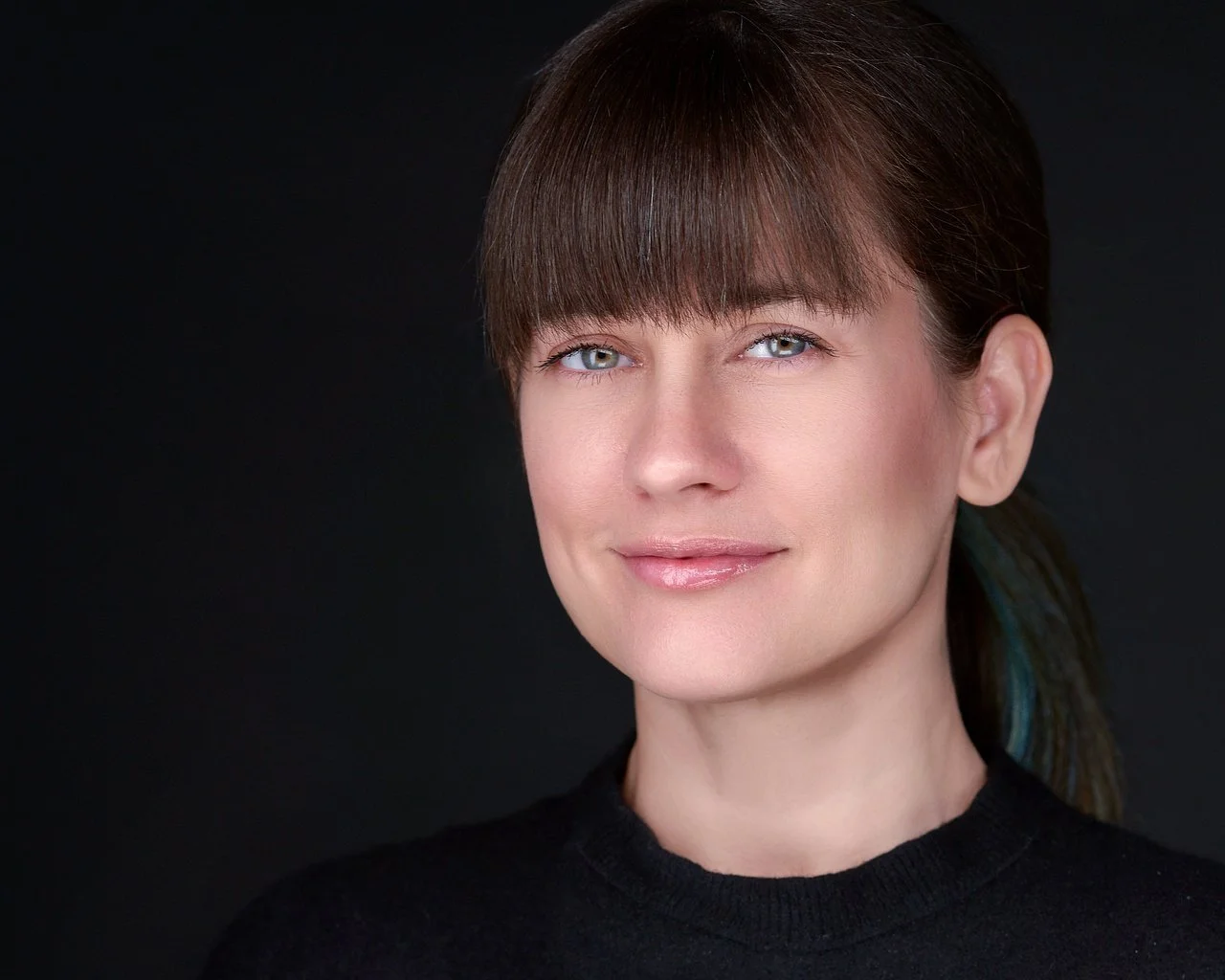 Portrait of a woman with brown hair and blue eyes against a black background.
