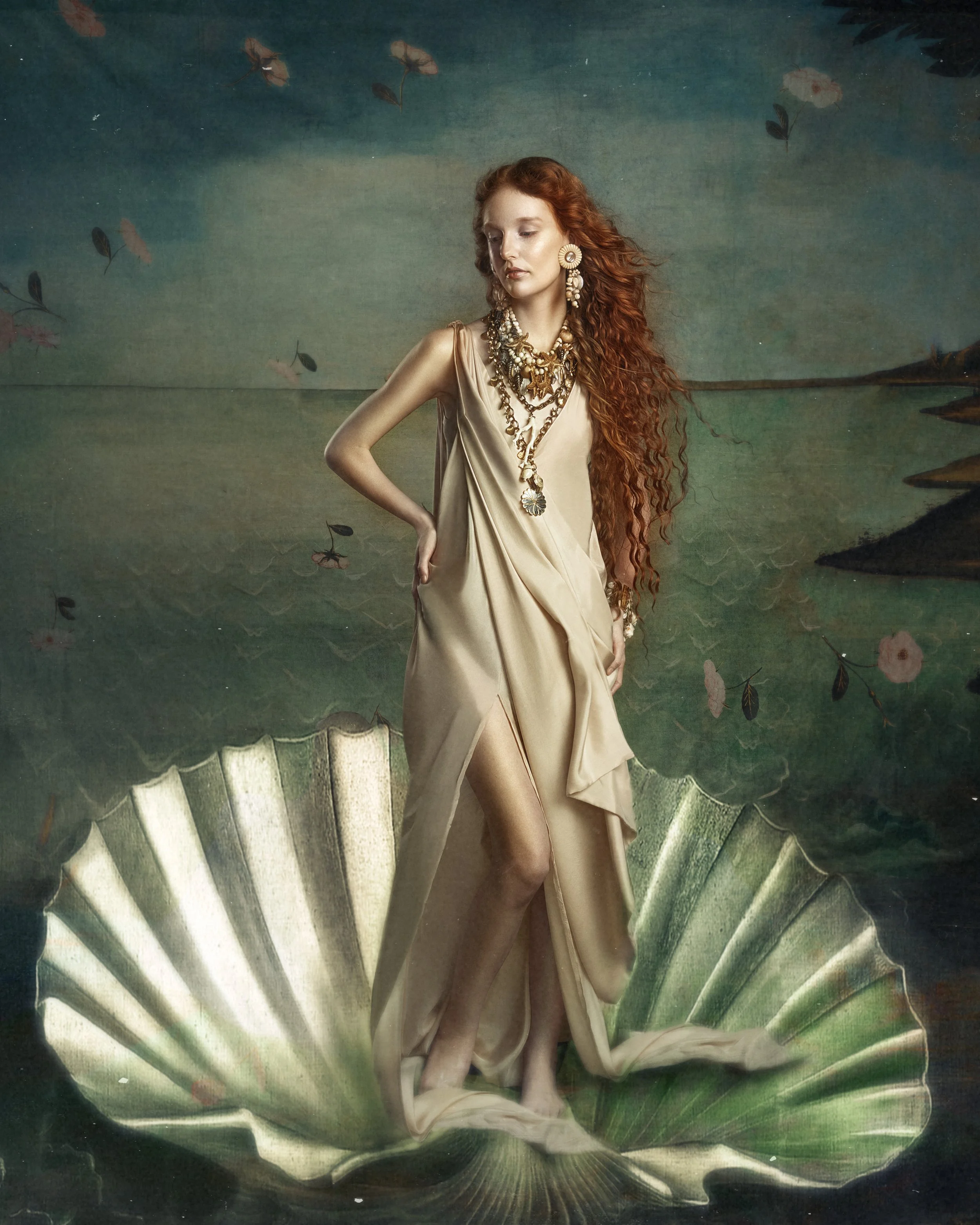A woman with long curly red hair standing on a large seashell, wearing a flowing beige dress and multiple ornate necklaces and earrings, with a painted landscape background.