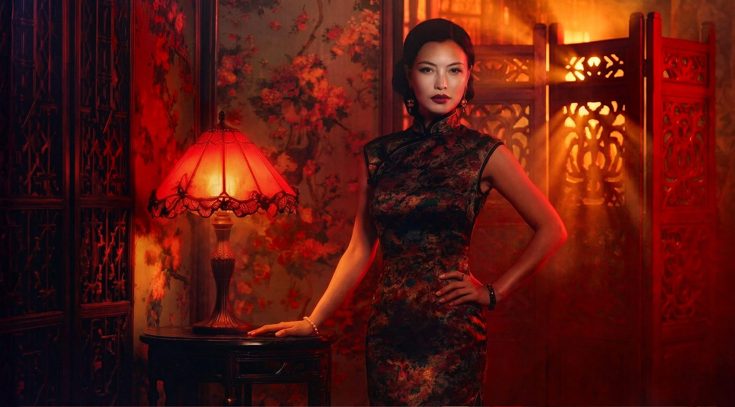 A woman in a traditional Chinese-style dress standing next to a table with a red lamp in a dimly lit room with Asian decor and red floral wallpaper.