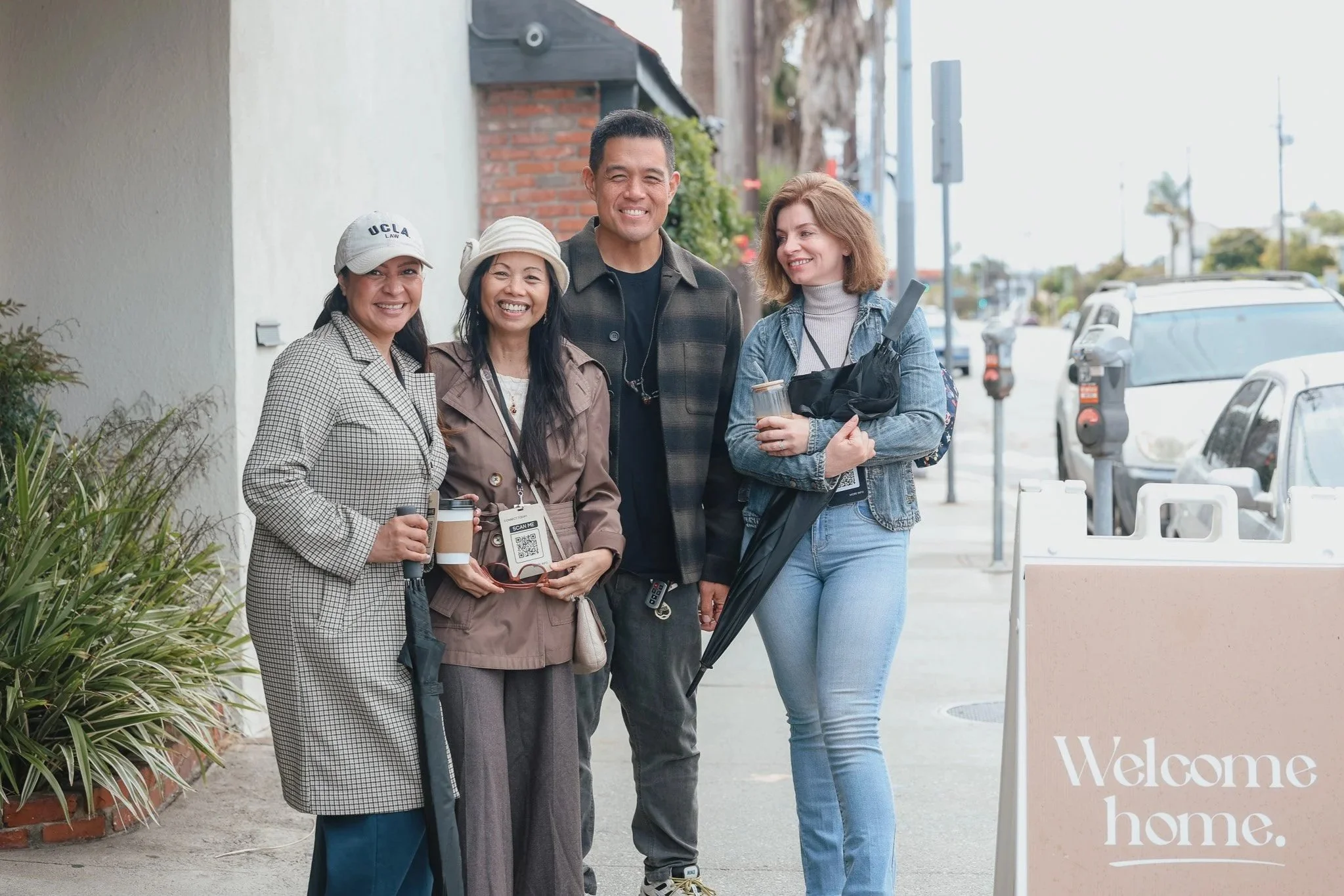 Group of four diverse people standing outdoors, smiling, with plants and a blue sign in the background.