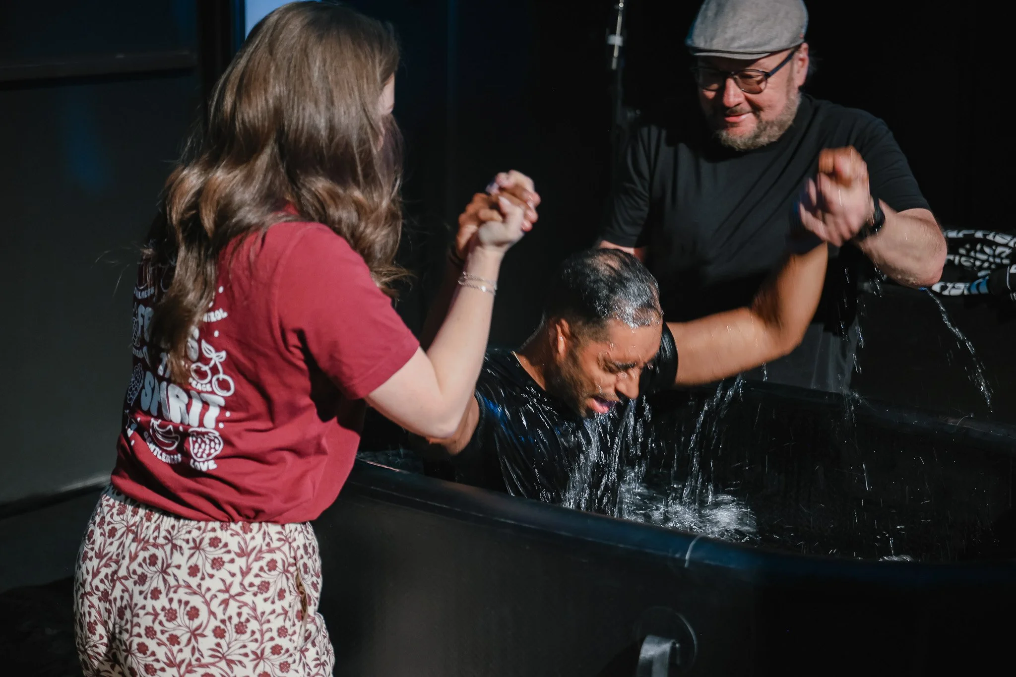 A woman is praying in a baptismal pool while being surrounded by her pastors during her baptism.