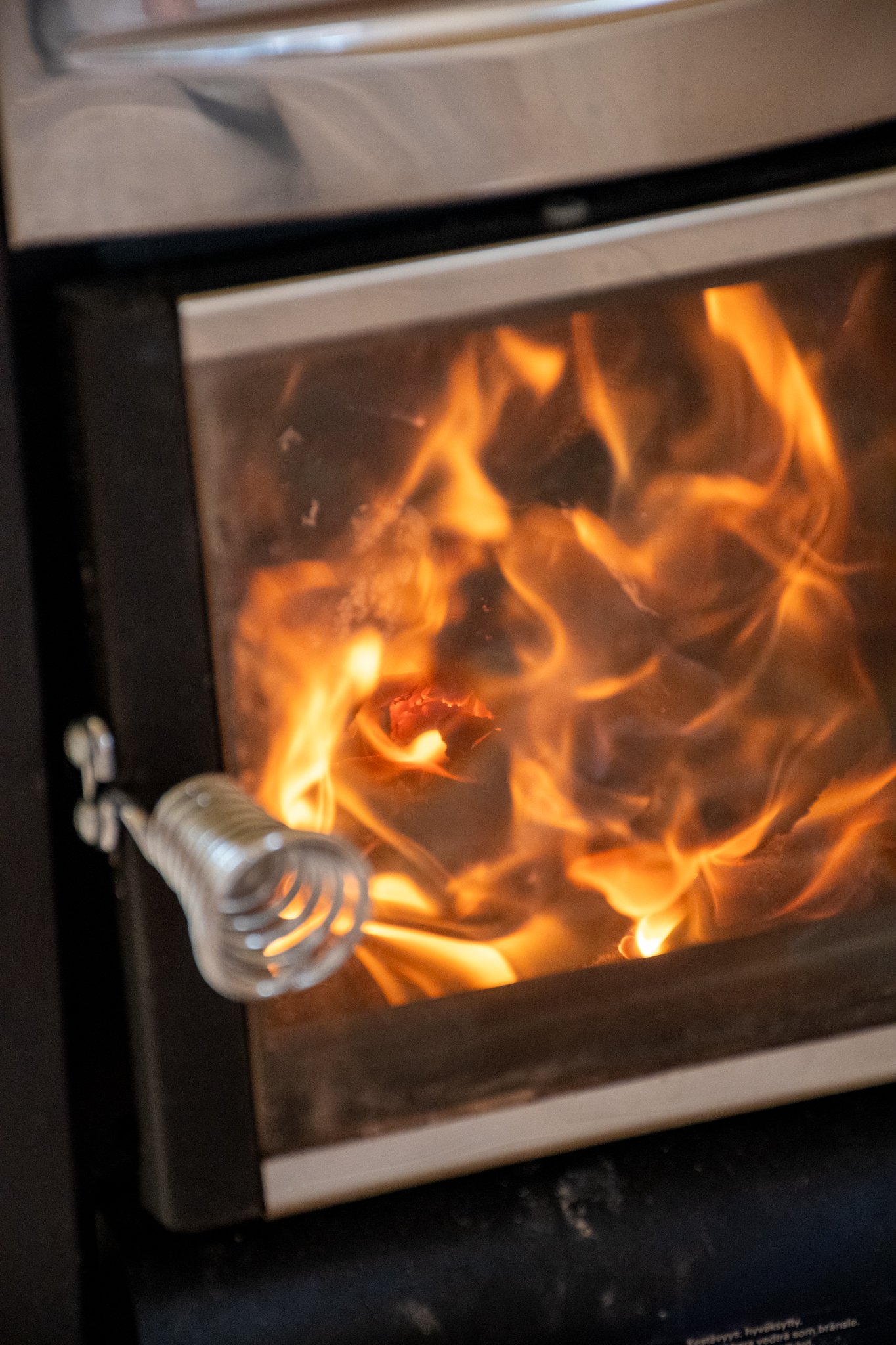 A small metal stove with glass door, showing bright orange and yellow flames inside.
