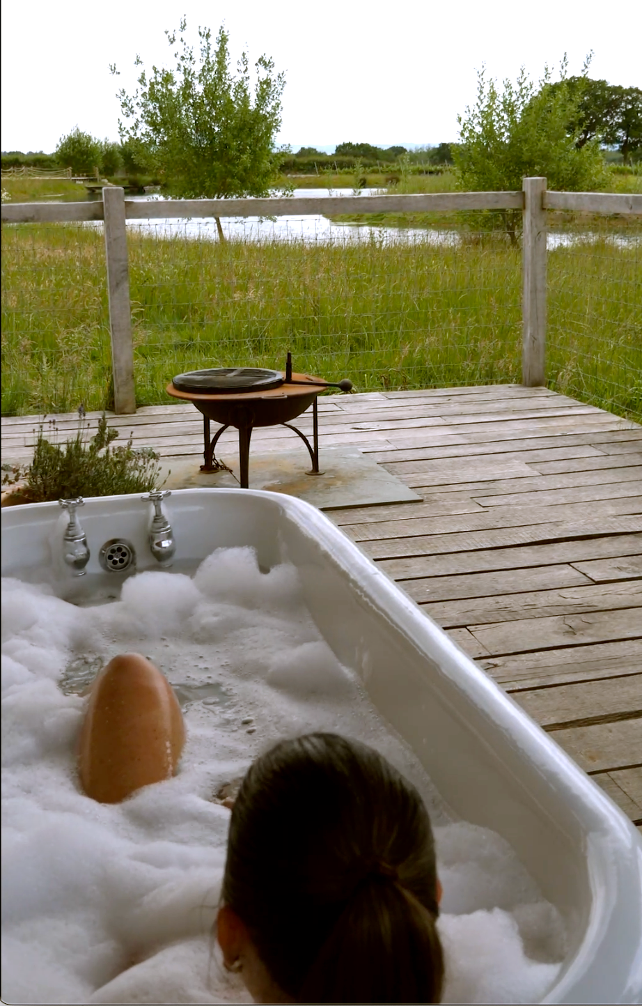 Outdoor bath on a wooden deck at Wagtail Retreat, overlooking vineyard and lake with sunset sky