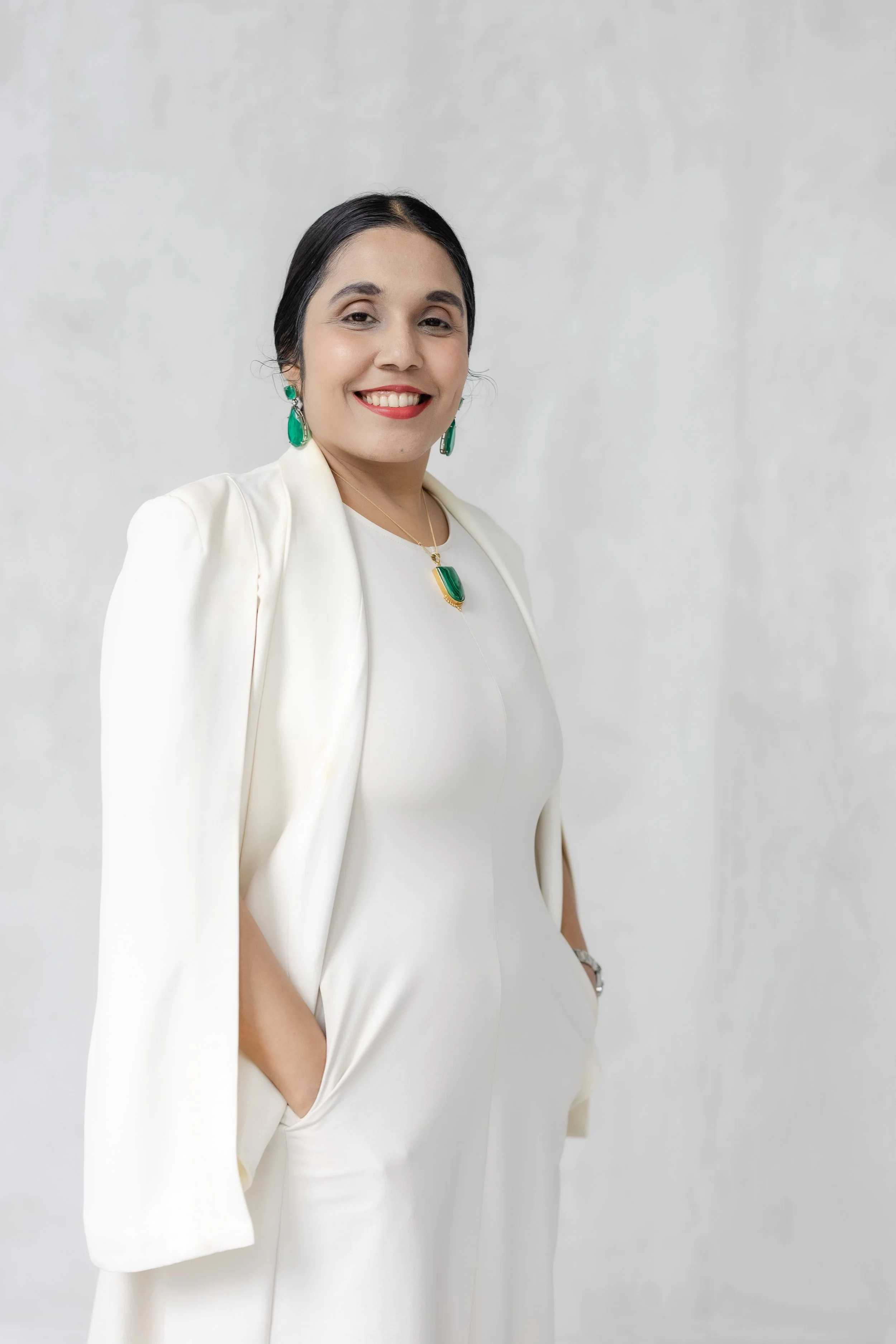 Smiling woman in a white blazer and blouse wearing green earrings and a matching pendant necklace
