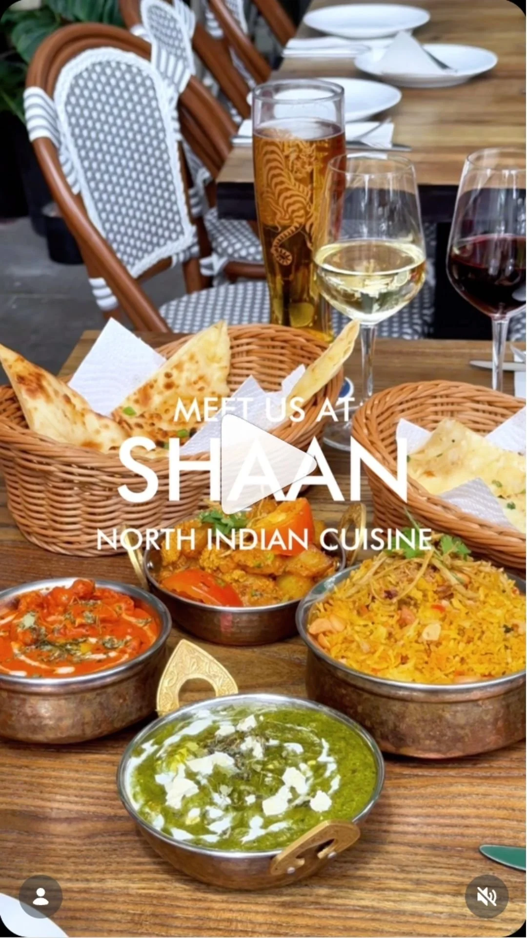 A table with Indian dishes, including curries, rice, naan bread, and beverages such as wine and beer, set with white plates and utensils. Text overlay says 'Meet us at Shaan North Indian Cuisine.'