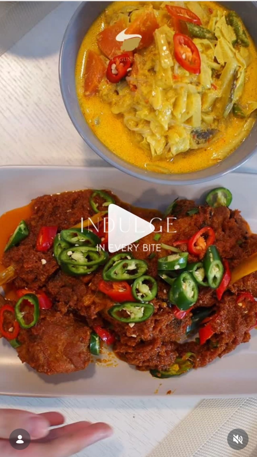 Two plates of food, one with a yellow curry containing vegetables and slices of red chili peppers, and the other with fried meat topped with sliced green and red chili peppers and garnished with chopped green onions.