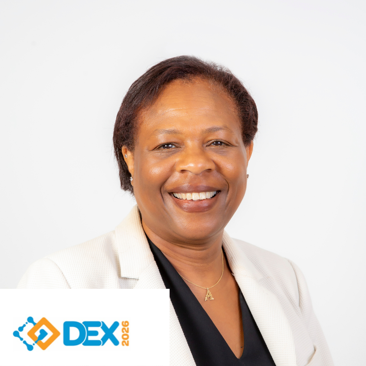 A smiling woman in a white blazer and black top, wearing a gold necklace with an 'A' pendant, against a white background with a DEX 2026 logo in the bottom left corner.
