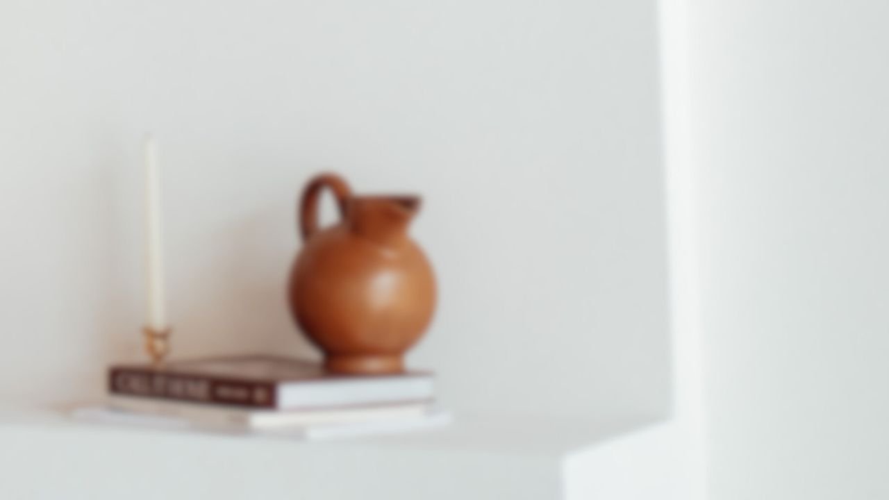 Blurred image of a brown jug on stacked books with a candle.