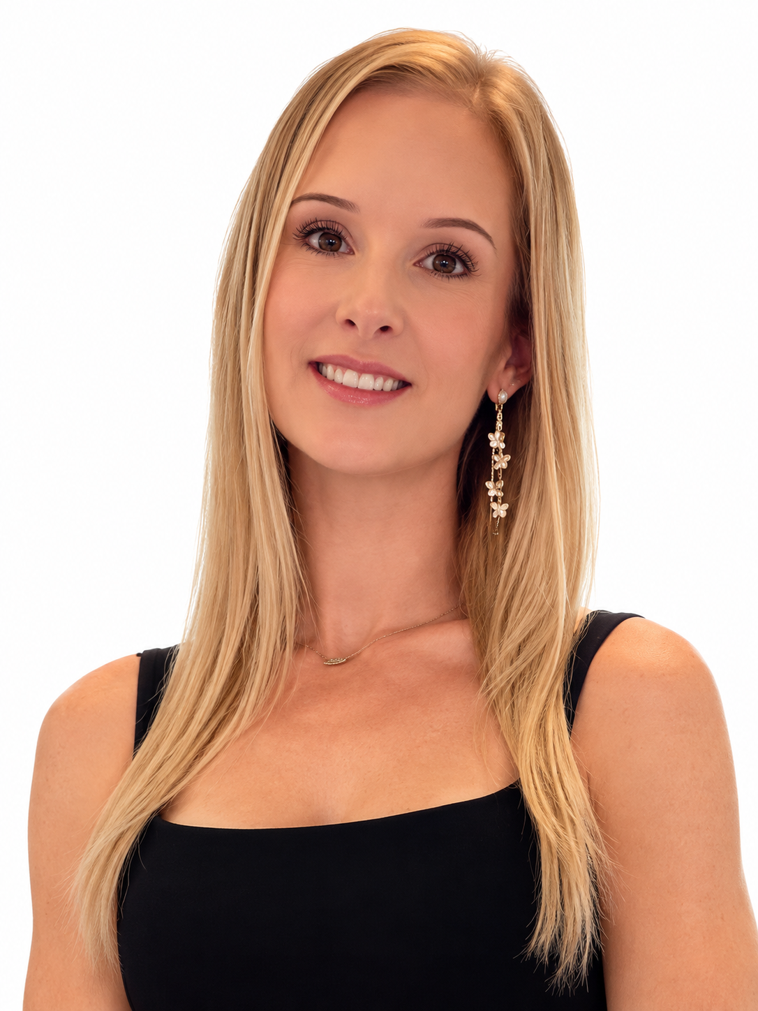 A woman with long blonde hair, wearing a black top and dangling earrings, smiling at the camera against a white background.