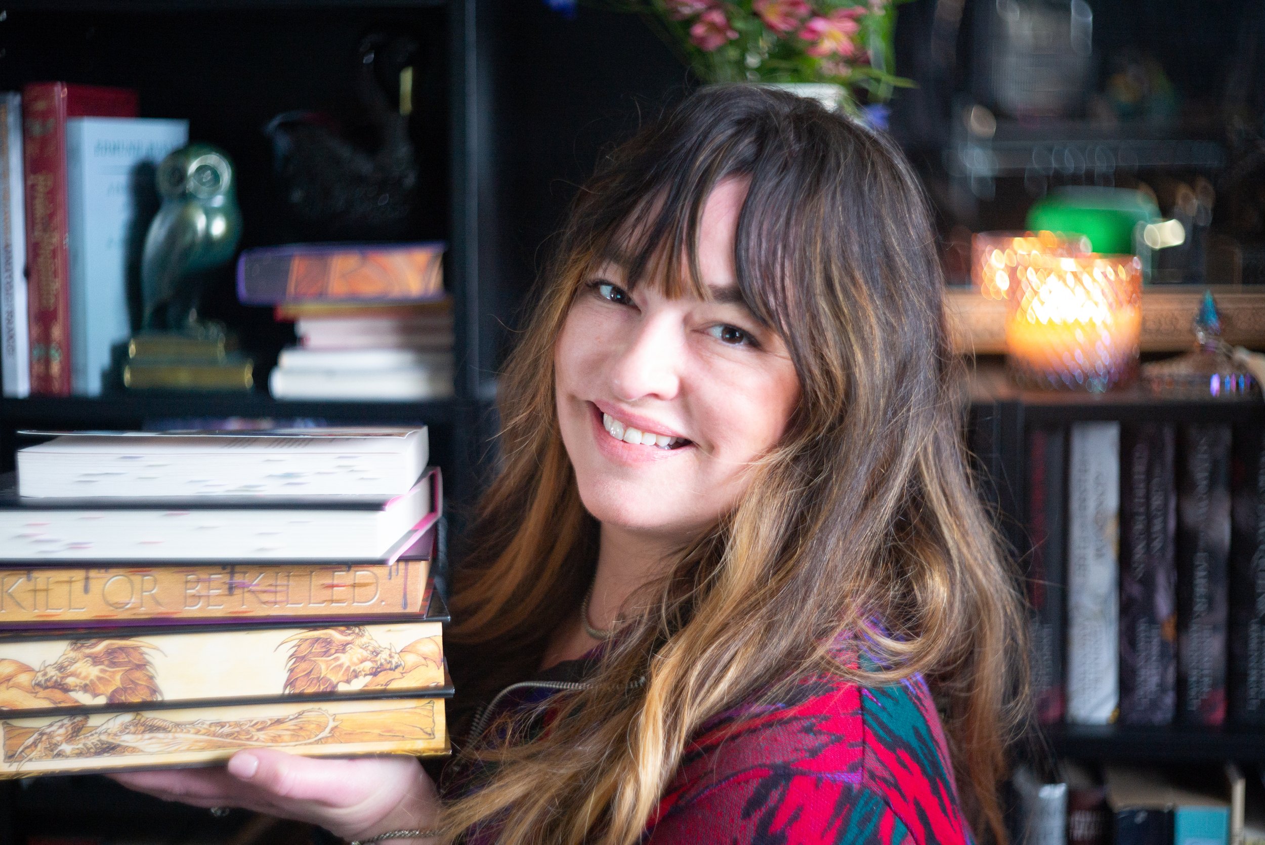 Photo of Cassandra holding a stack of physical fantasy romance books