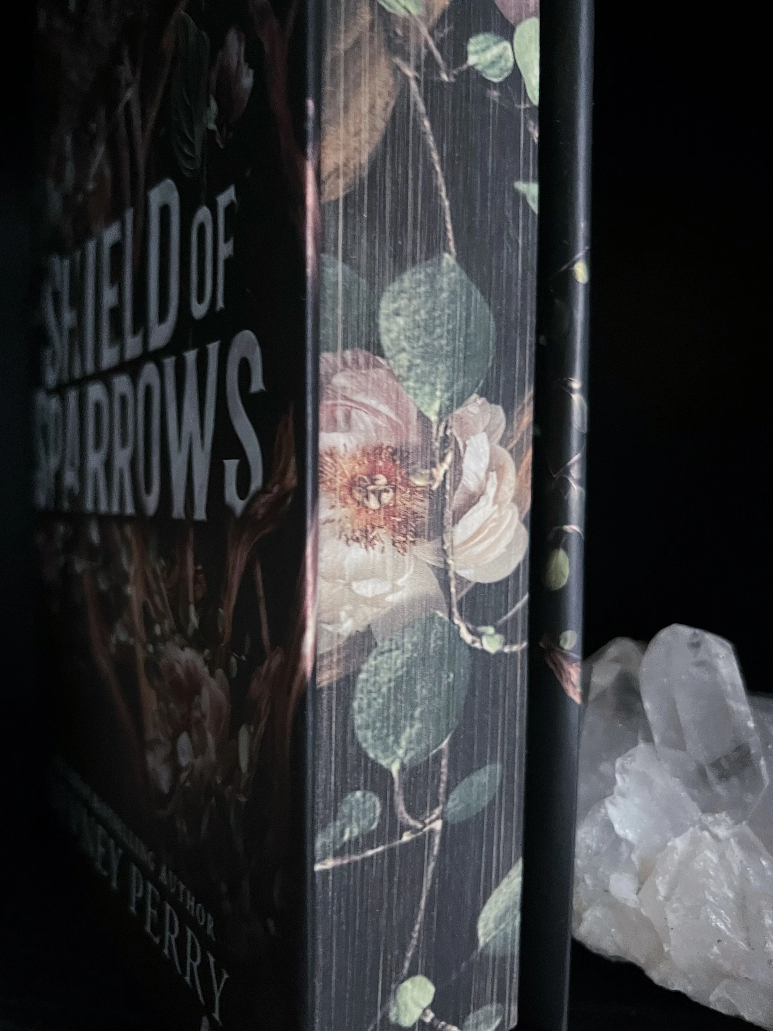 This is a close-image of the Limited Edition of Shield of Sparrows featuring a black background and flowers with branches and leaves.