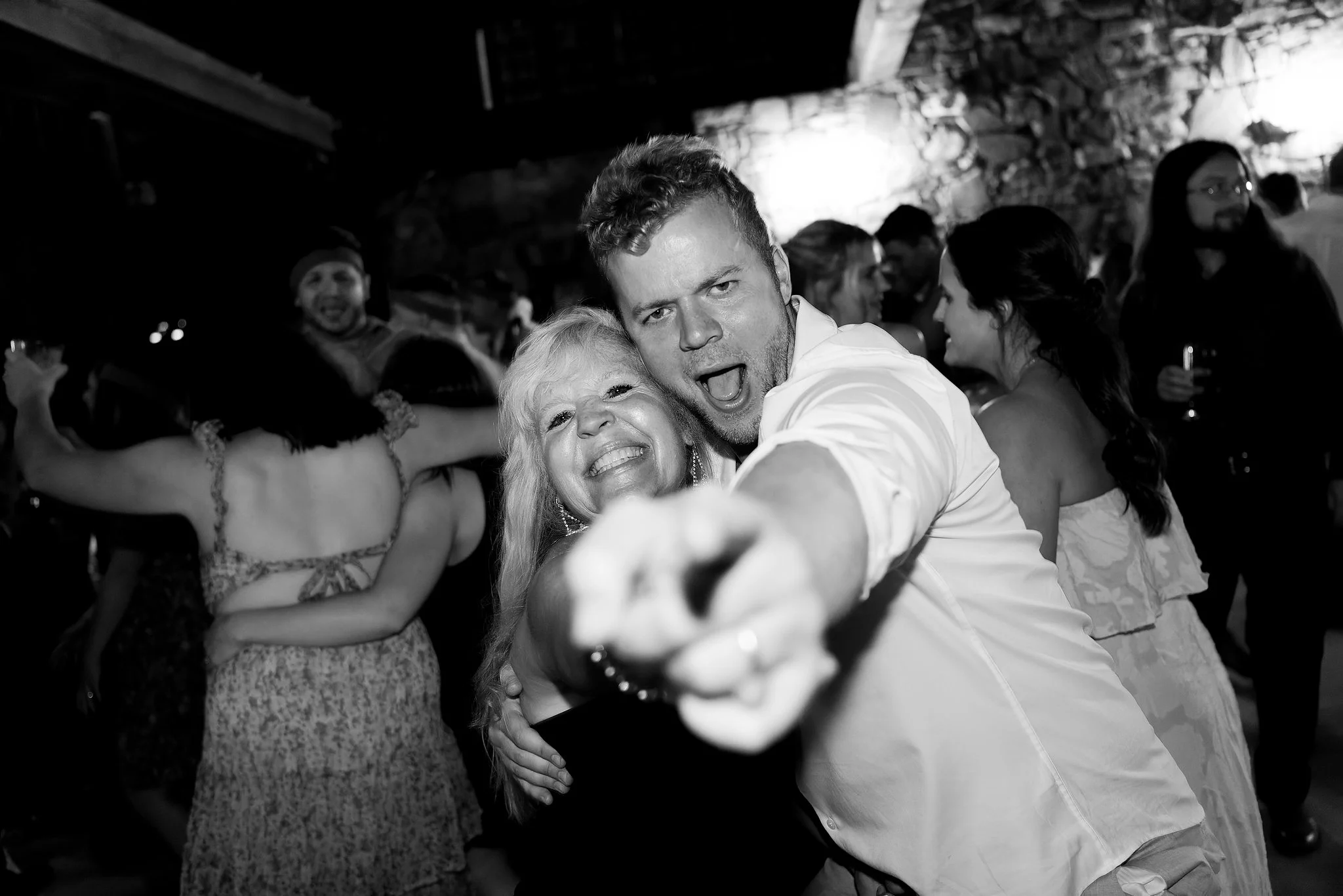 People dancing at a lively party or celebration, smiling and embracing each other.