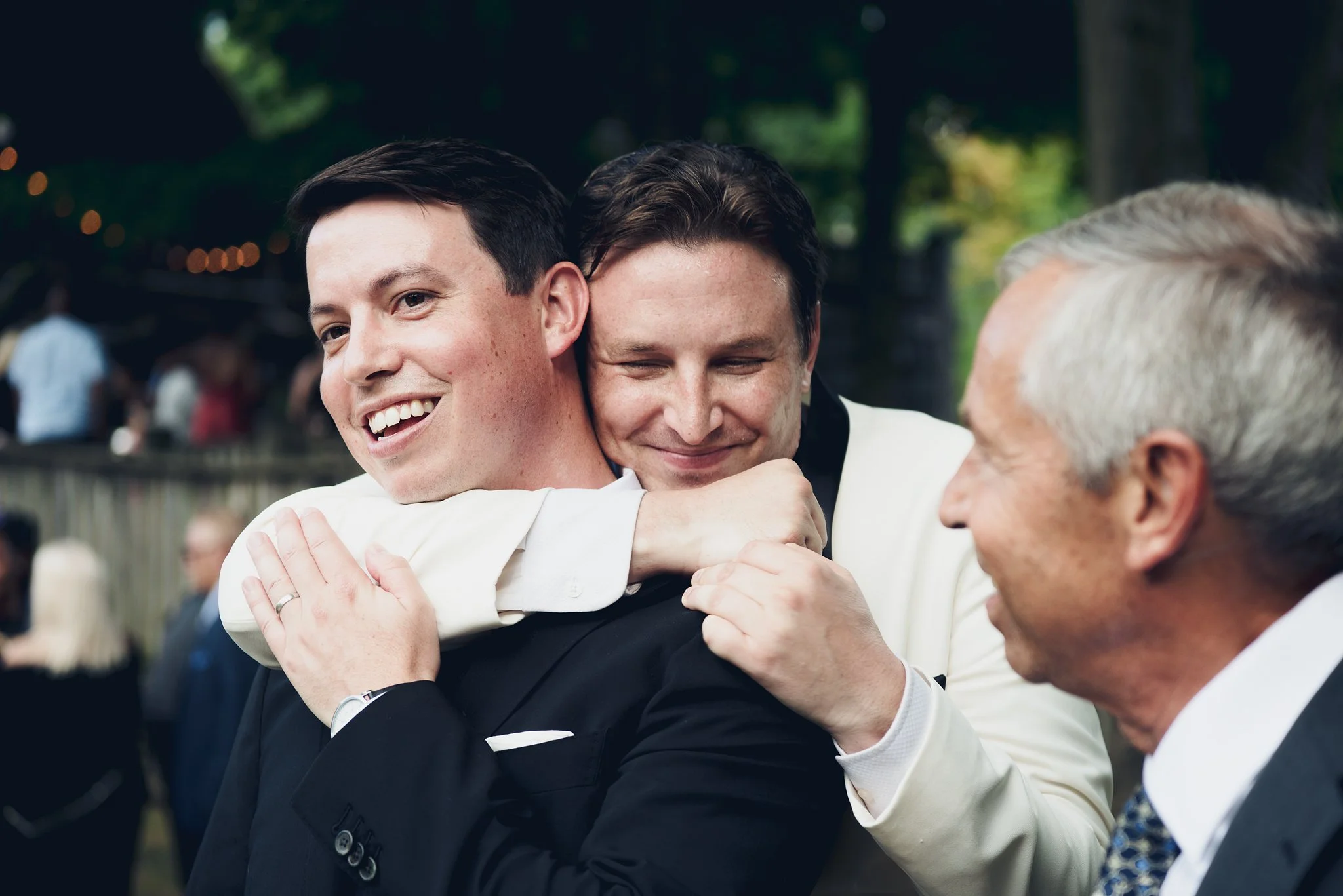 Three men are hugging each other at an outdoor event, smiling and appear happy.