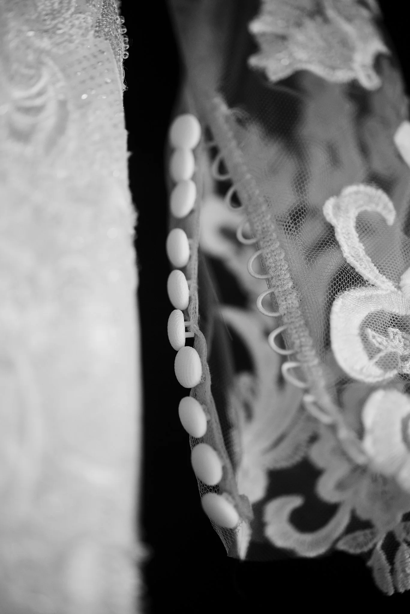 Close-up of a lace fabric with small buttons or beads along the edge, in black and white.