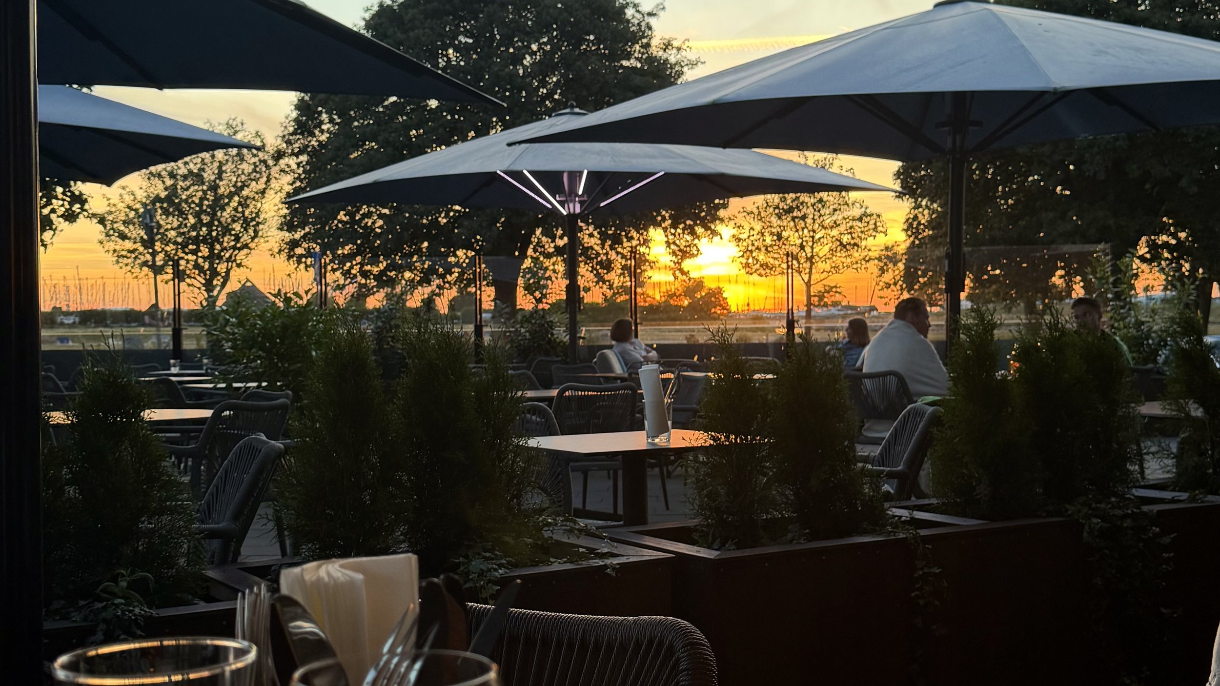 En bartender står bakom en bar med en bakgrund av hyllor fyllda med olika sorters sprit och glas, samt en öppen bar med olika flaskor och dekorationer.