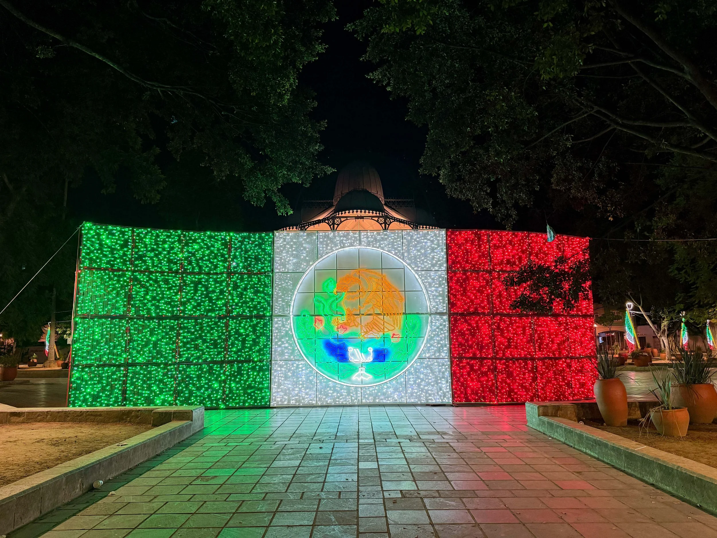 Oaxaca's illuminated government building decorated with colorful lights, patriotic figures and large green, white and red letters spelling “México” for Mexican Independence Day.