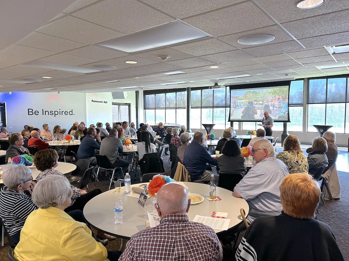 Guests seated at round tables watch a presentation during the fundraising event.