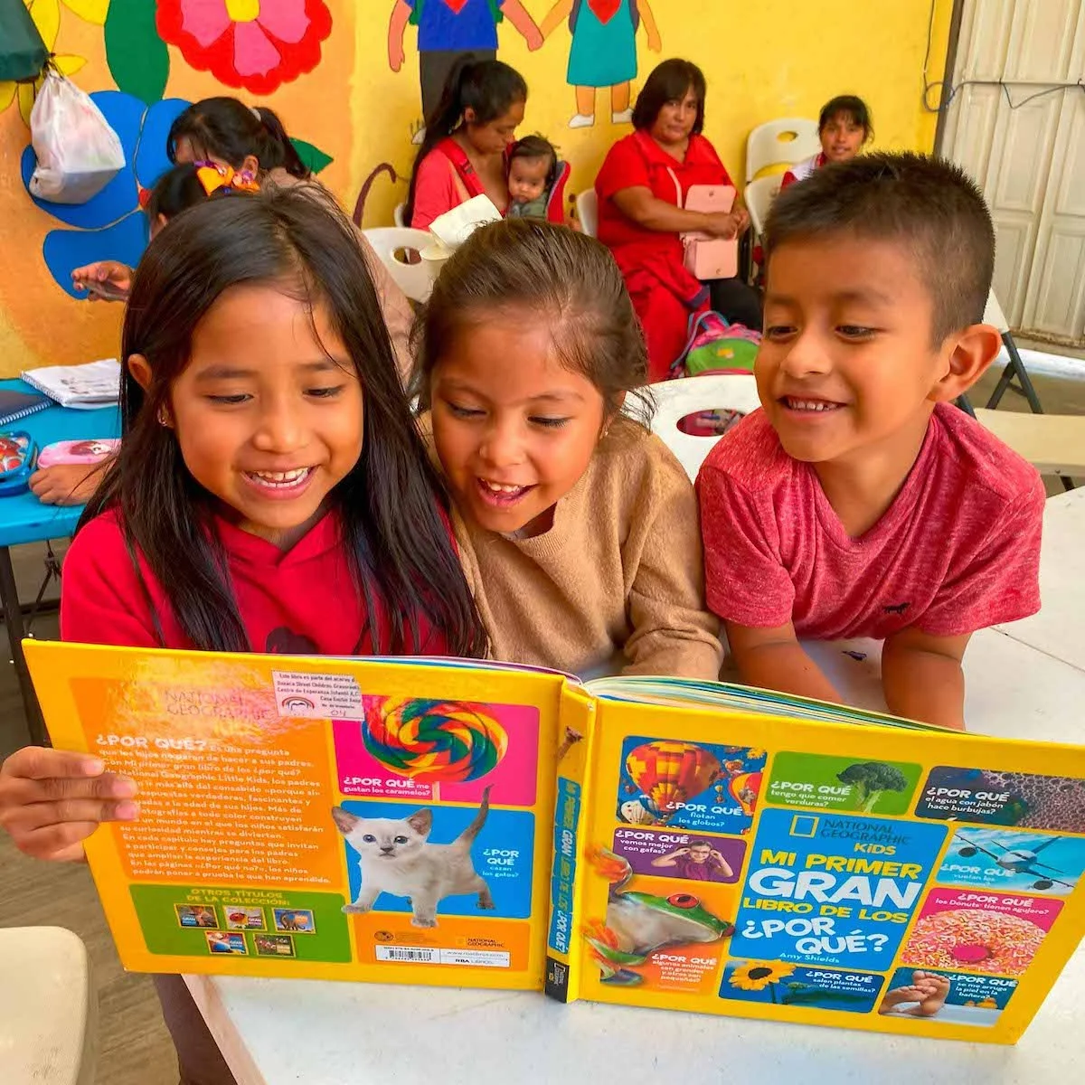 Three kindergarten children smiling while discovering reading together.