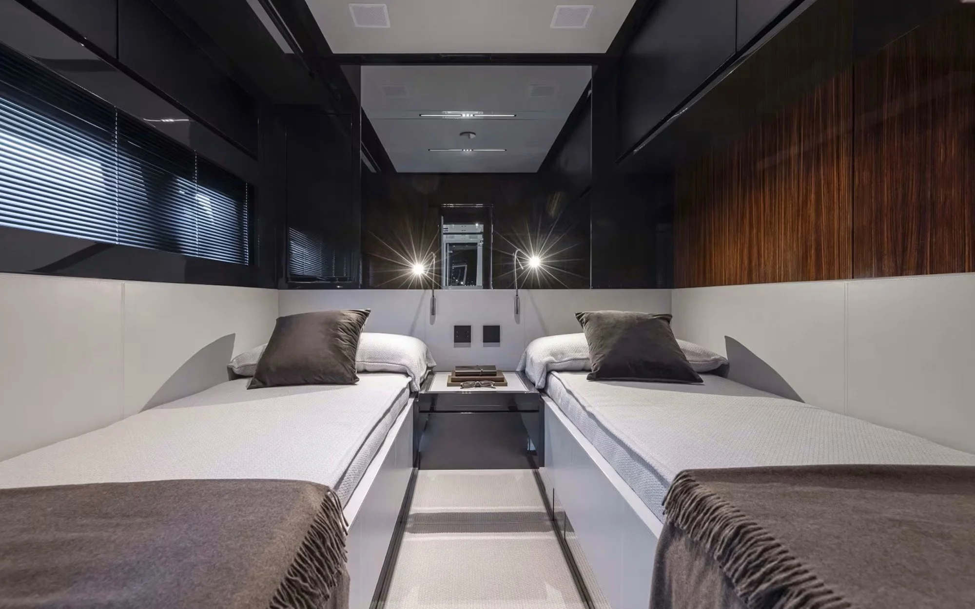 Modern bedroom with two single beds, dark pillows, a small black side table, wall-mounted reading lights, a mirror, and window blinds.