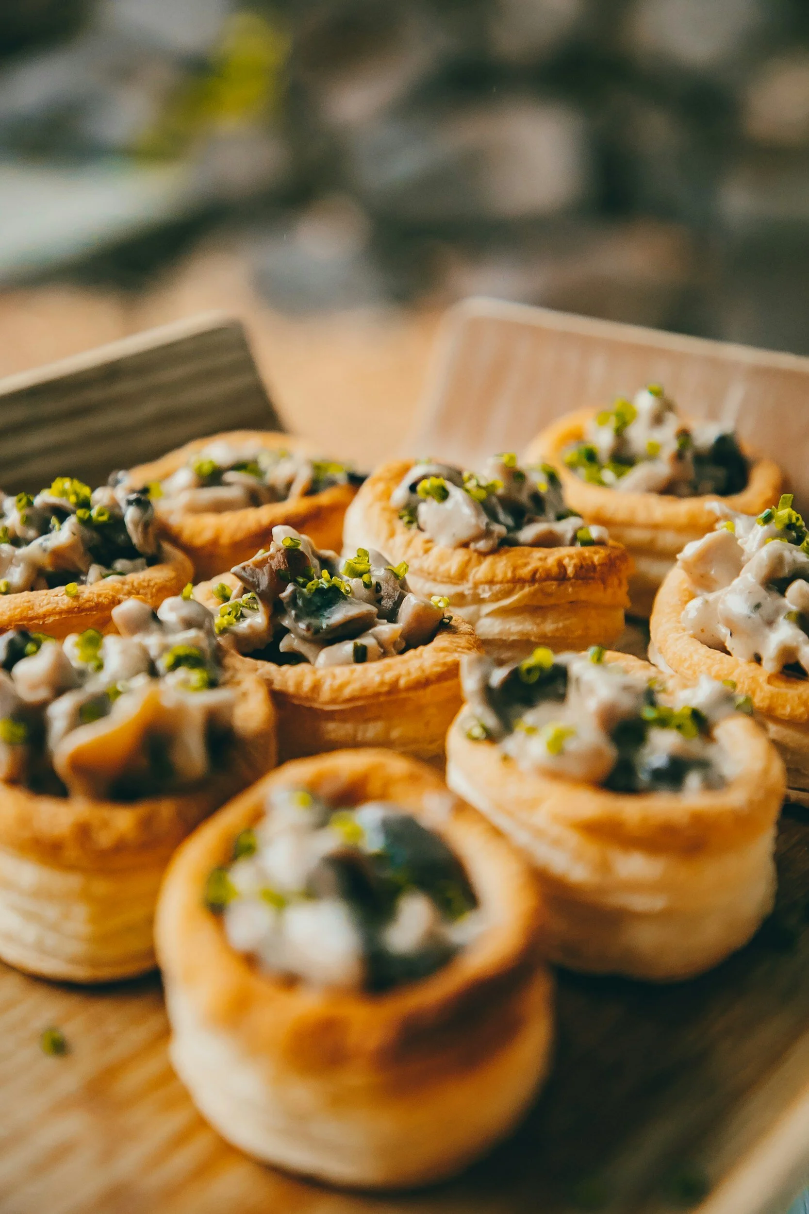 Appetizers with pastry shells filled with a creamy mushroom and chive mixture on a wooden tray.