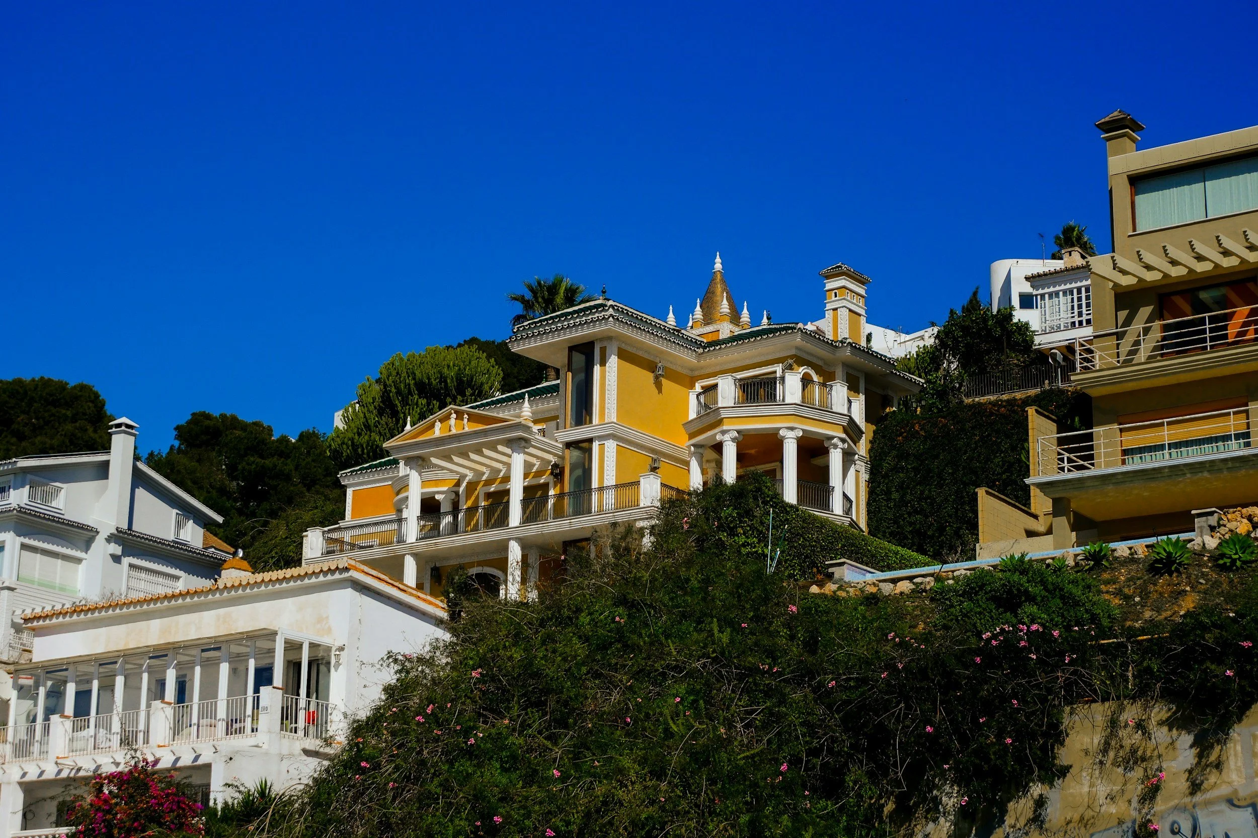 Colorful hillside houses with terraces and a castle-like church spire under a clear blue sky.