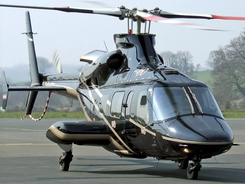 A black helicopter on an airport tarmac with trees in the background.