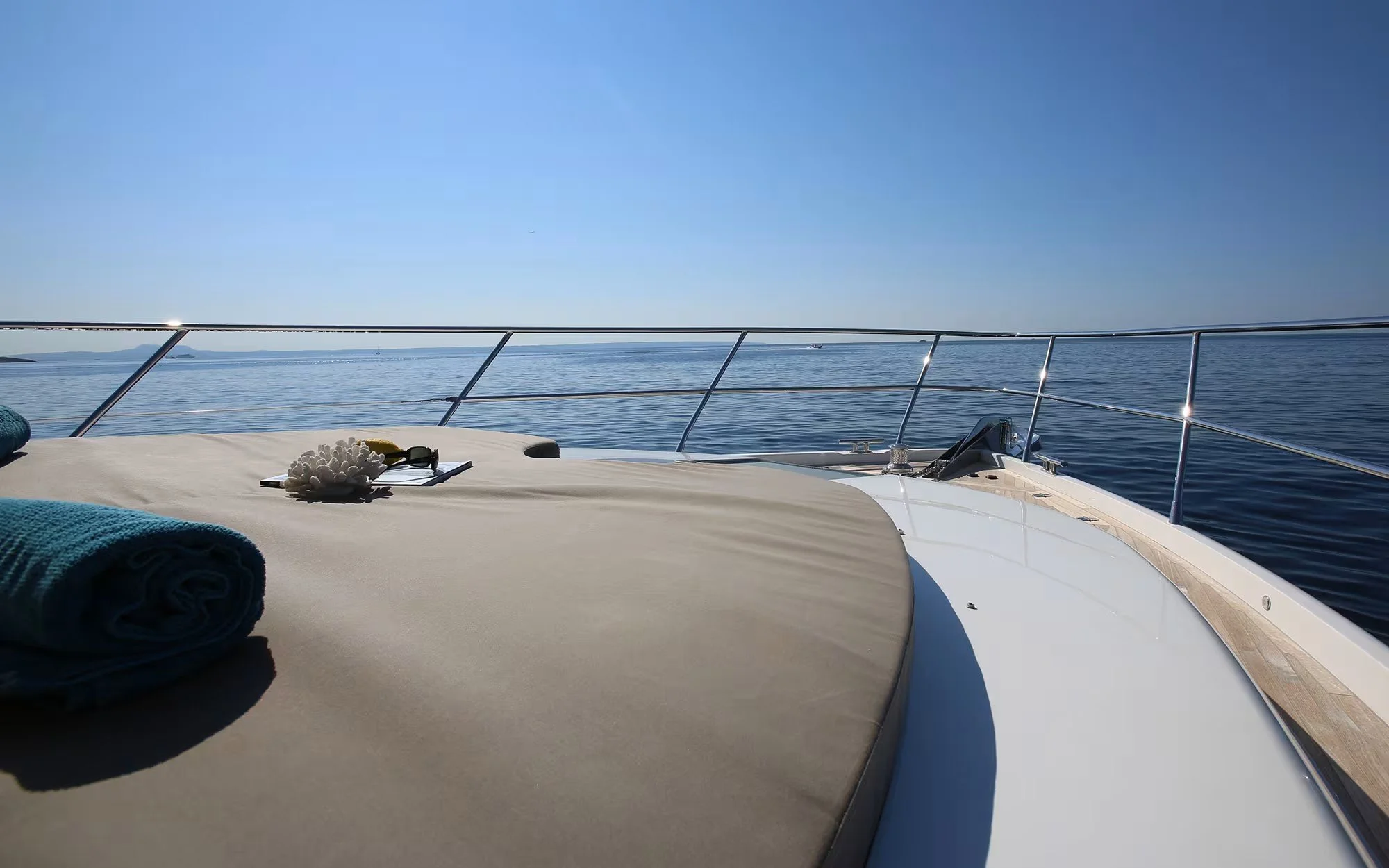 View from a yacht's deck showing a blue ocean, clear sky, with towel and seashell decor on the deck.