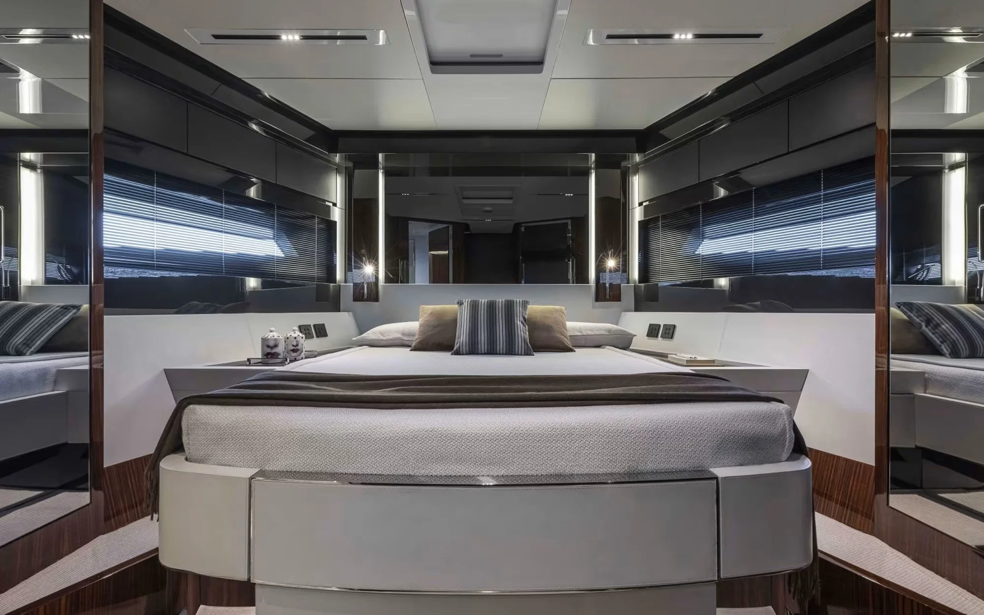 Luxurious bedroom with a sleek modern design, featuring a large bed with a variety of pillows, mirrored walls, and large windows with blinds.