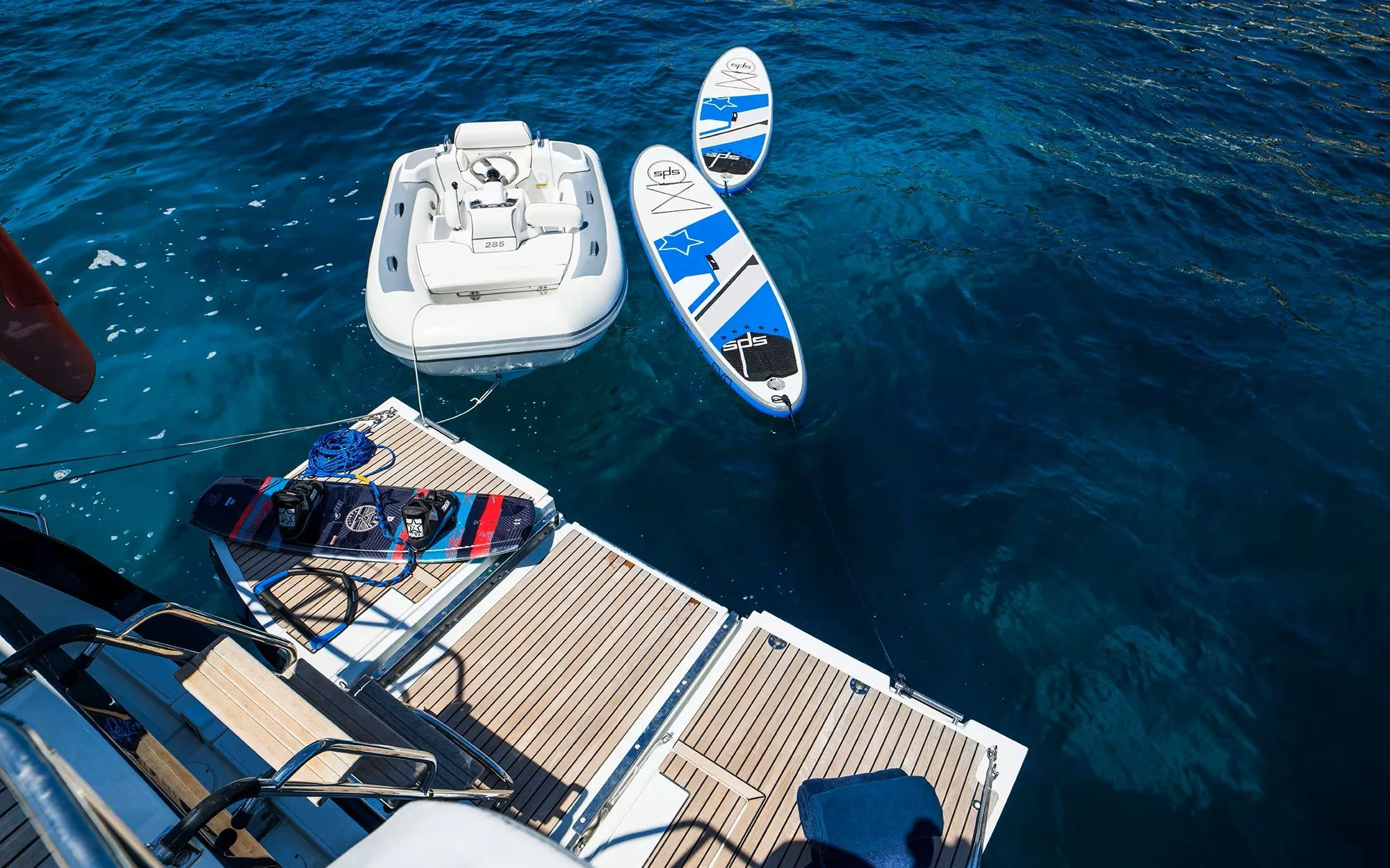 View from a boat showing two stand-up paddleboards, a small inflatable boat, and a boat deck with equipment on calm water.