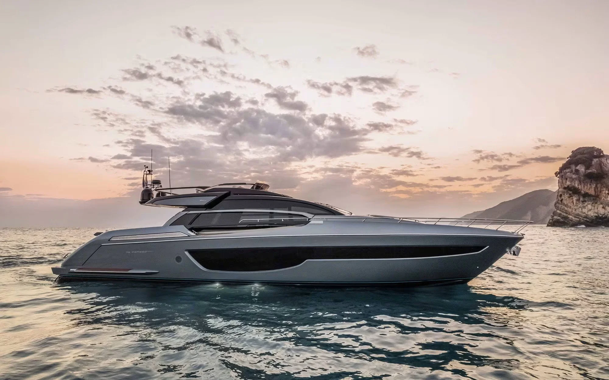 Luxury yacht sailing on the ocean at sunset, with cloudy sky and rocky island in the background.