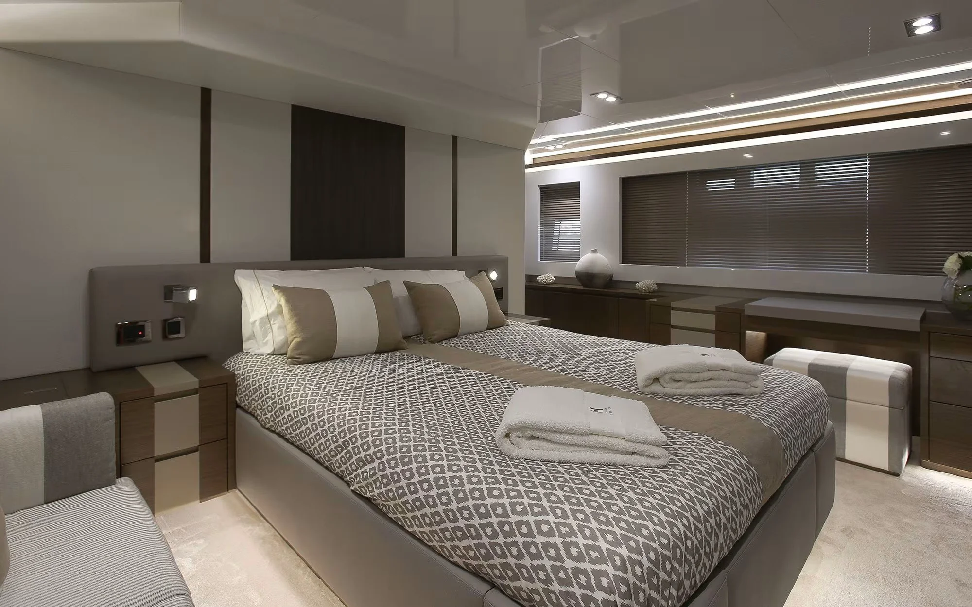 Modern hotel bedroom with a large bed, neutral-colored bedding, pillows, and fresh towels, with a desk and decorative vases along the window wall.