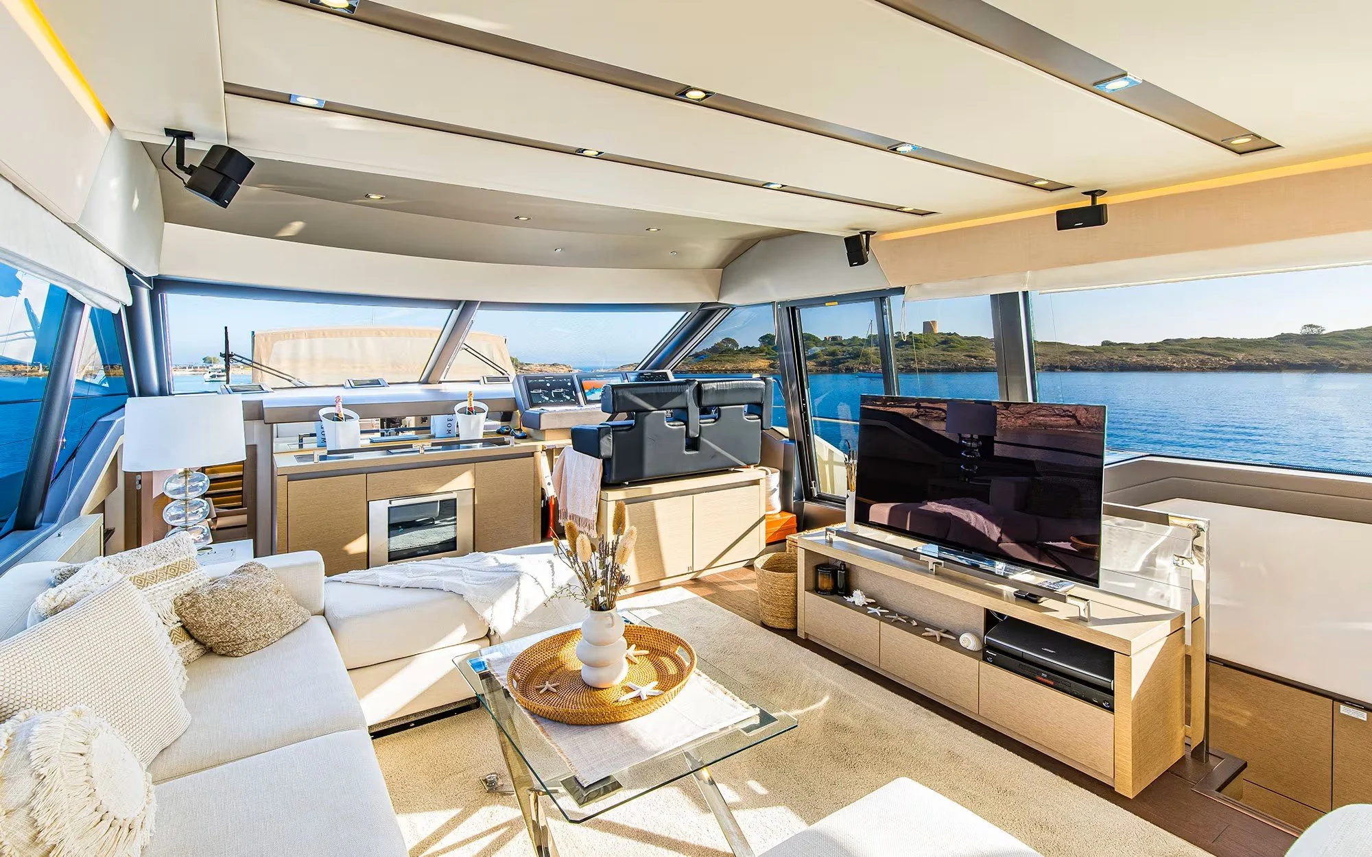 Luxurious boat interior with large windows showing a water view, modern furniture, a flat-screen TV, and decorations.