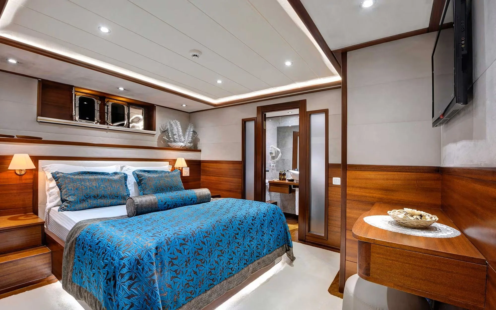 Hotel room with a bed, blue bedding, wooden furniture, and a bathroom visible through a door.