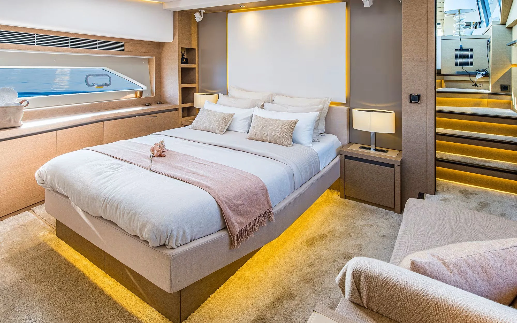 Modern cruise ship cabin with a large bed, decorative pillows, and a window with a view of the ocean.