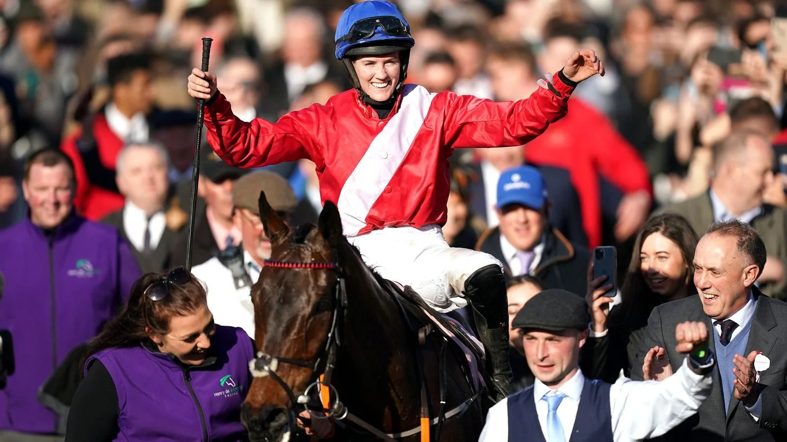 A female jockey celebrating on her horse after a race, surrounded by a crowd of spectators.