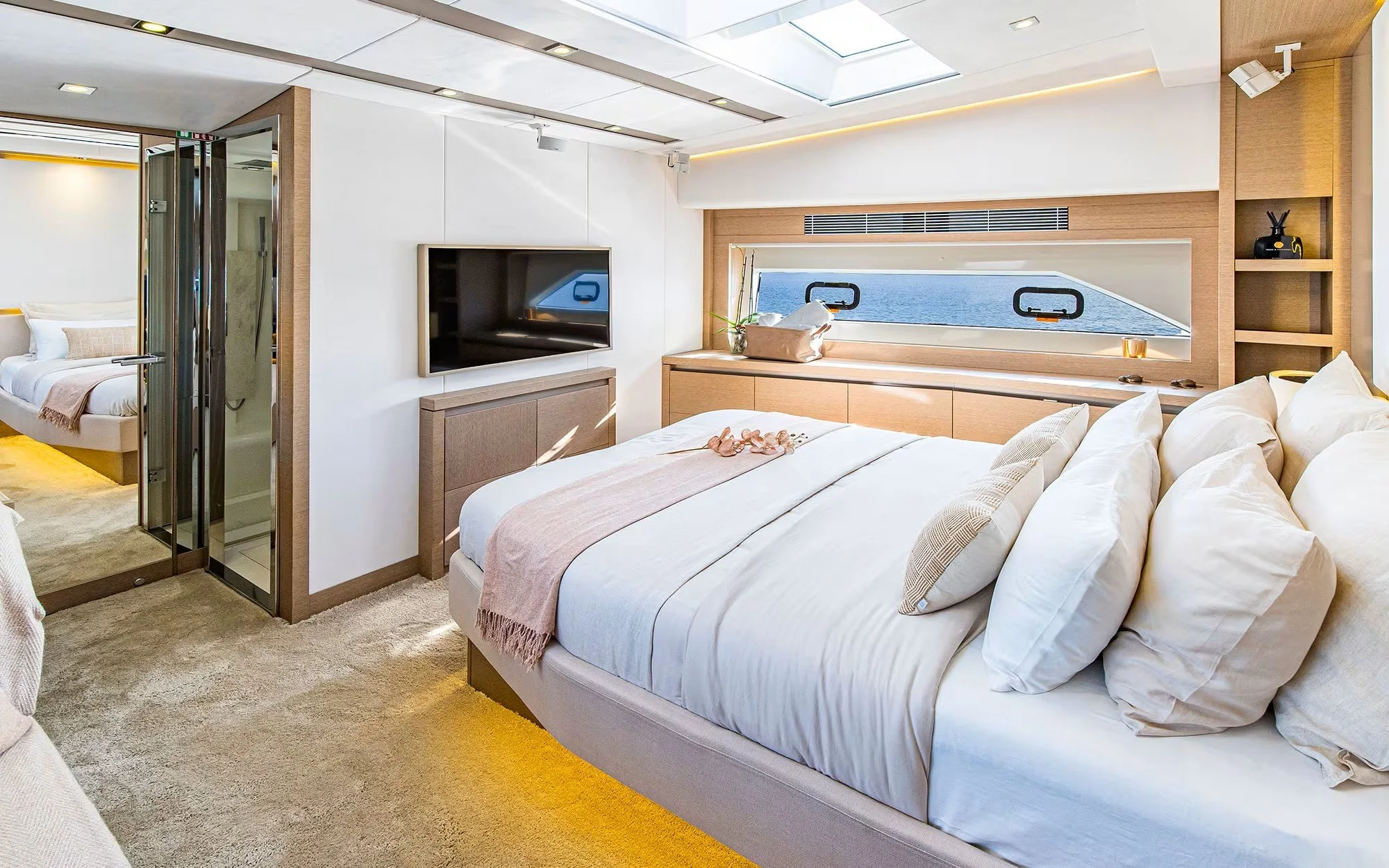 Luxurious bedroom with large bed, plush pillows, and a pink throw blanket, window overlooking the ocean, and a flat-screen TV mounted on the wall.