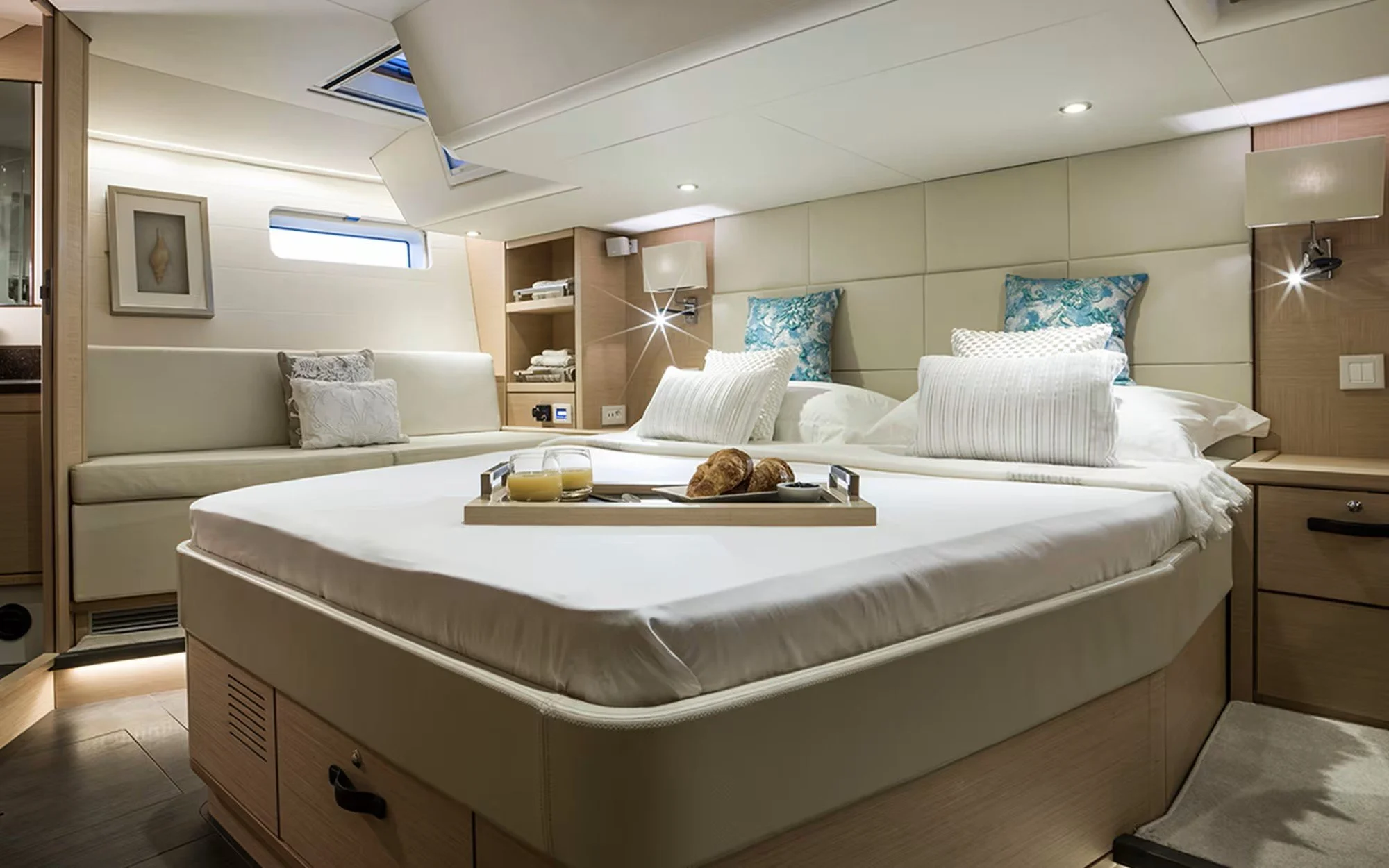 A bedroom with a large bed, breakfast tray, and pillows, on a boat or yacht with small windows and modern decor.