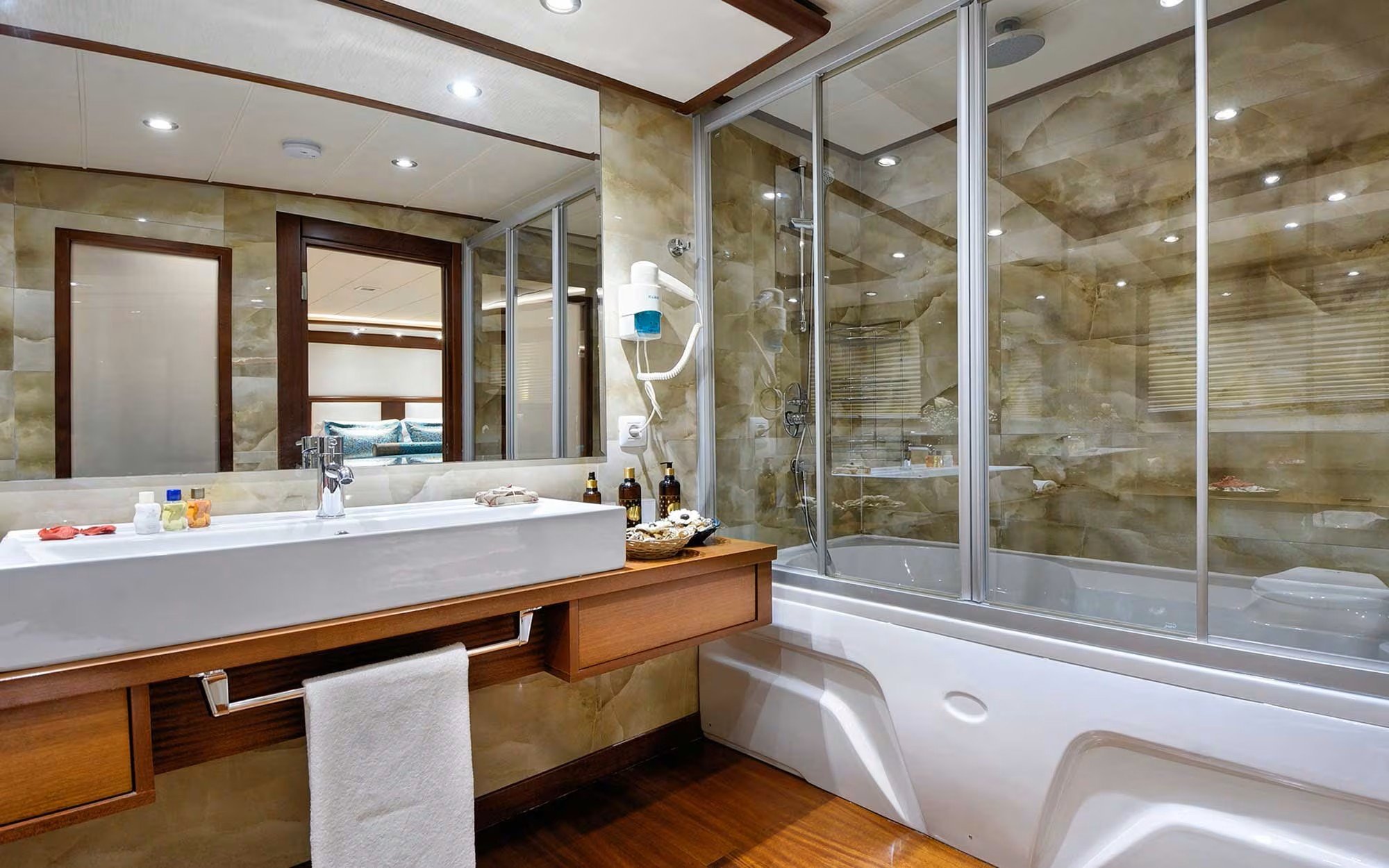 Modern bathroom with a large white sink, wooden vanity, a mirror, and a glass-enclosed shower with marble walls.
