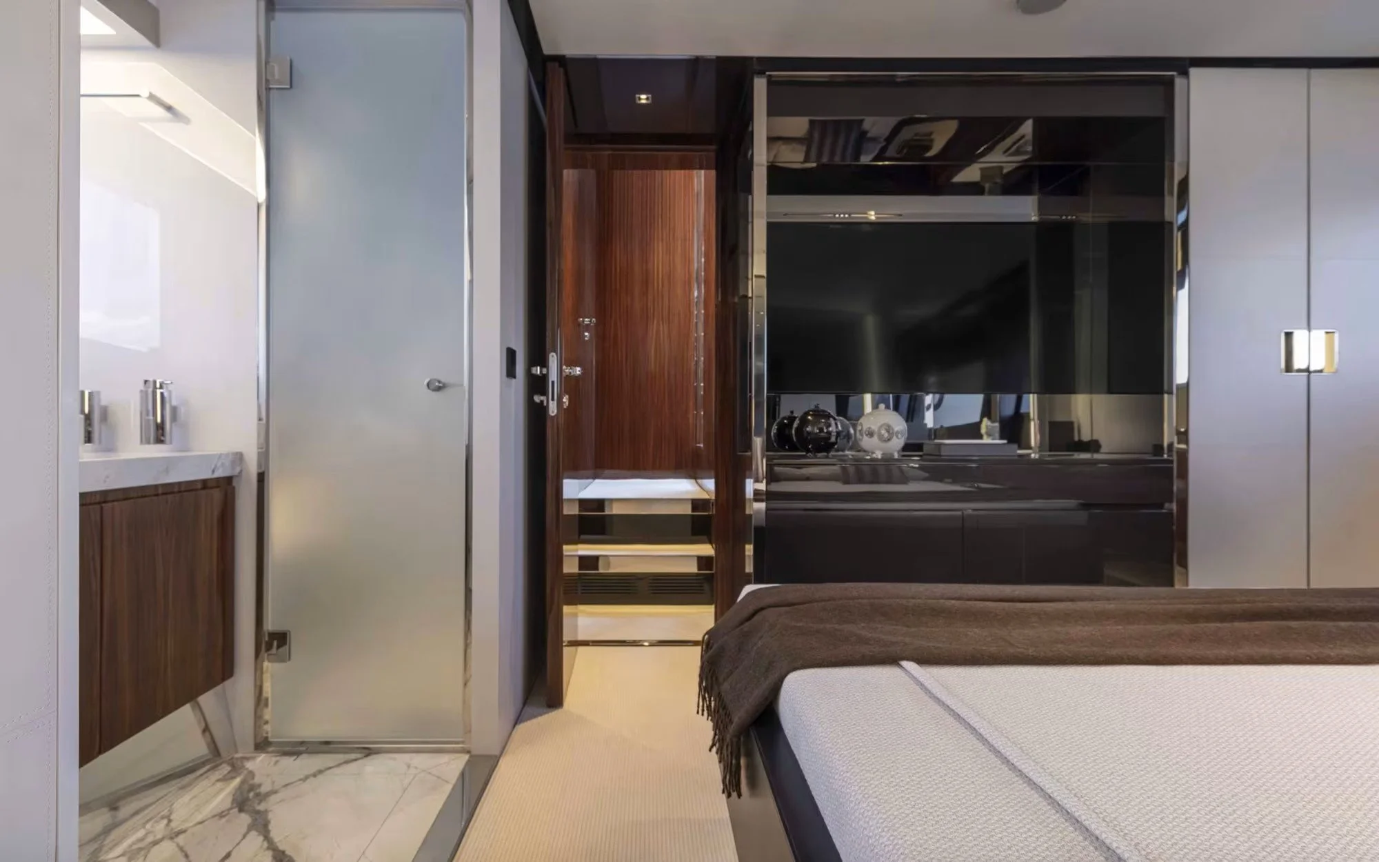 Modern hotel room interior with a bed, wooden and metallic cabinetry, and a bathroom vanity with a white marble countertop.