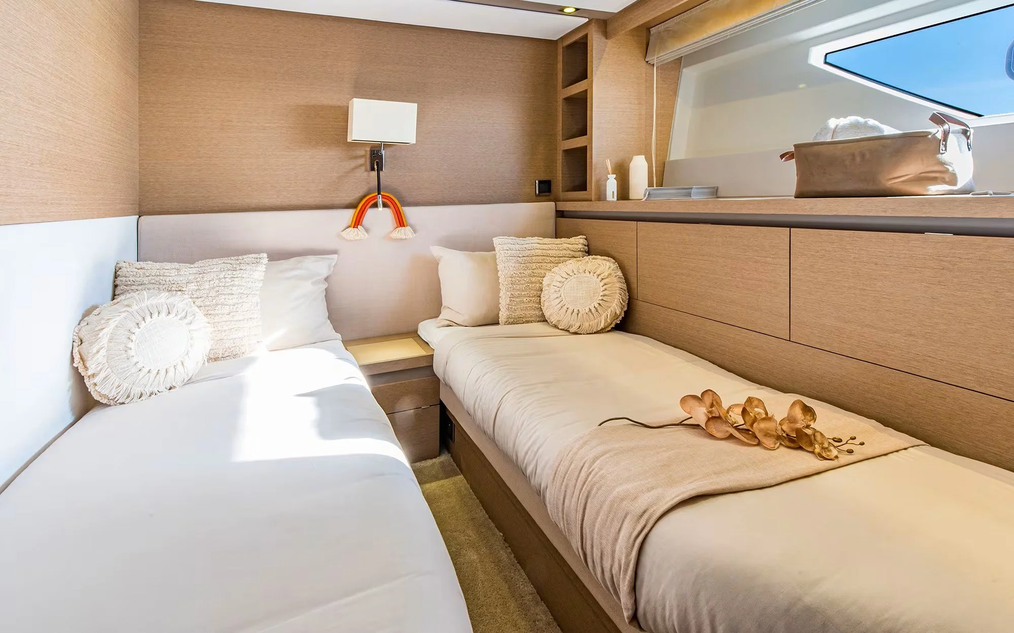 A cozy bedroom with two beds, white bedding, and decorative pillows. The room has wooden walls and built-in shelves, with sunlight streaming through a window.